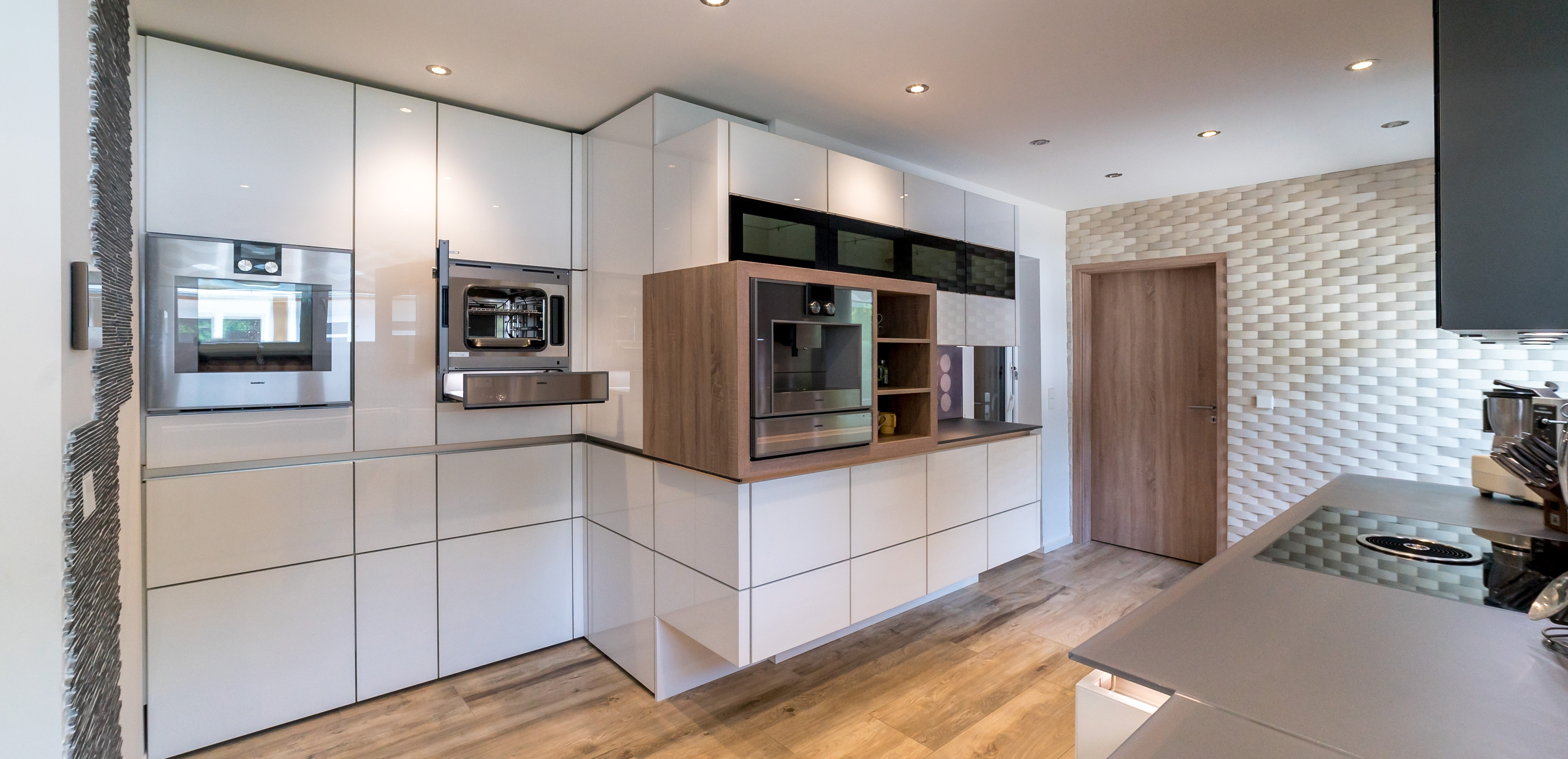 Moderne Küche mit weißen Schränken, Holzdetails und eingebauten Elektrogeräten.