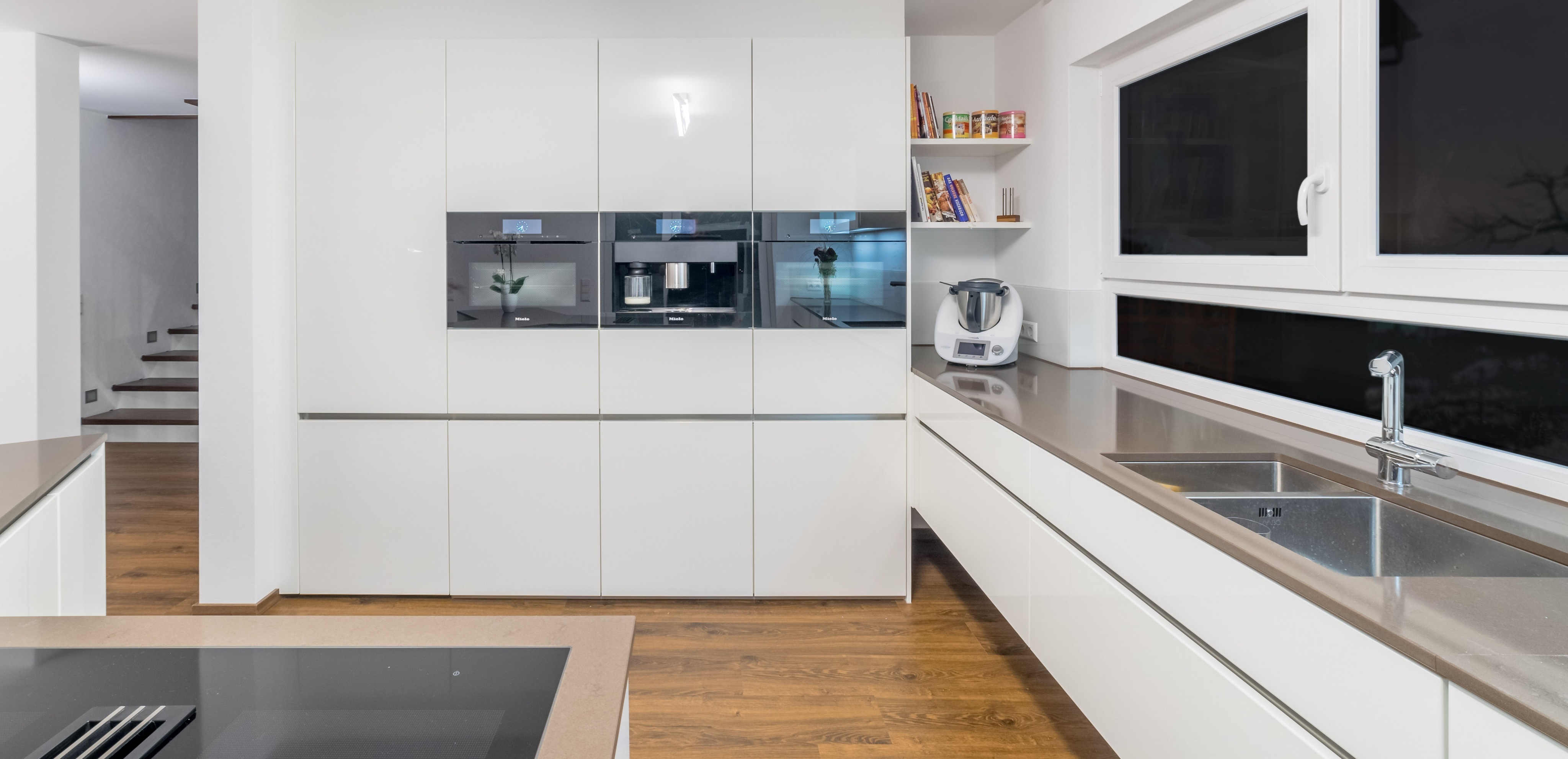 Moderne, helle Küche mit weißen Schränken, Edelstahlgeräten und großem Fenster.