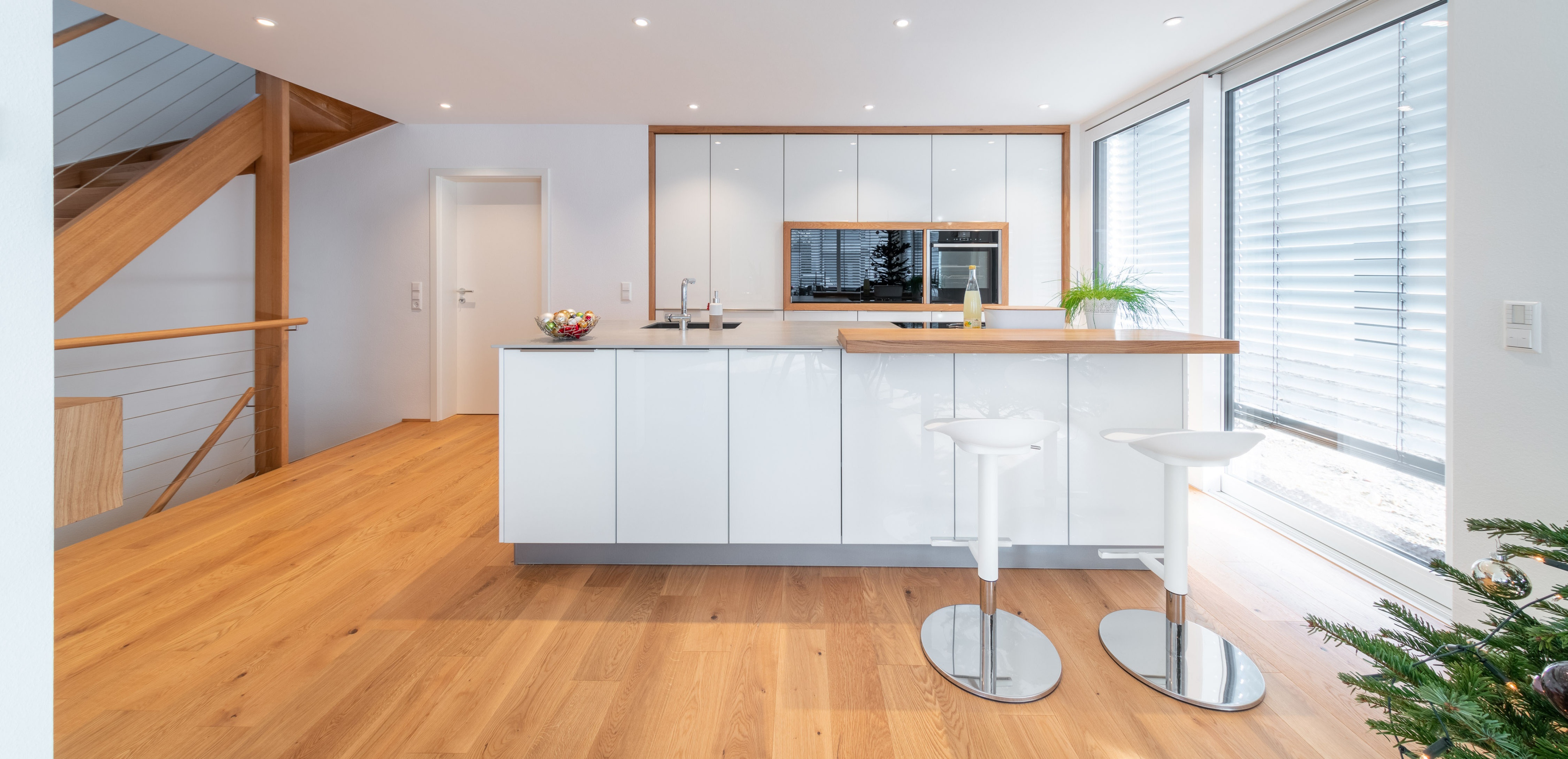 Moderne, helle Küche mit Kochinsel, Holzfußboden und großen Fenstern mit Jalousien.