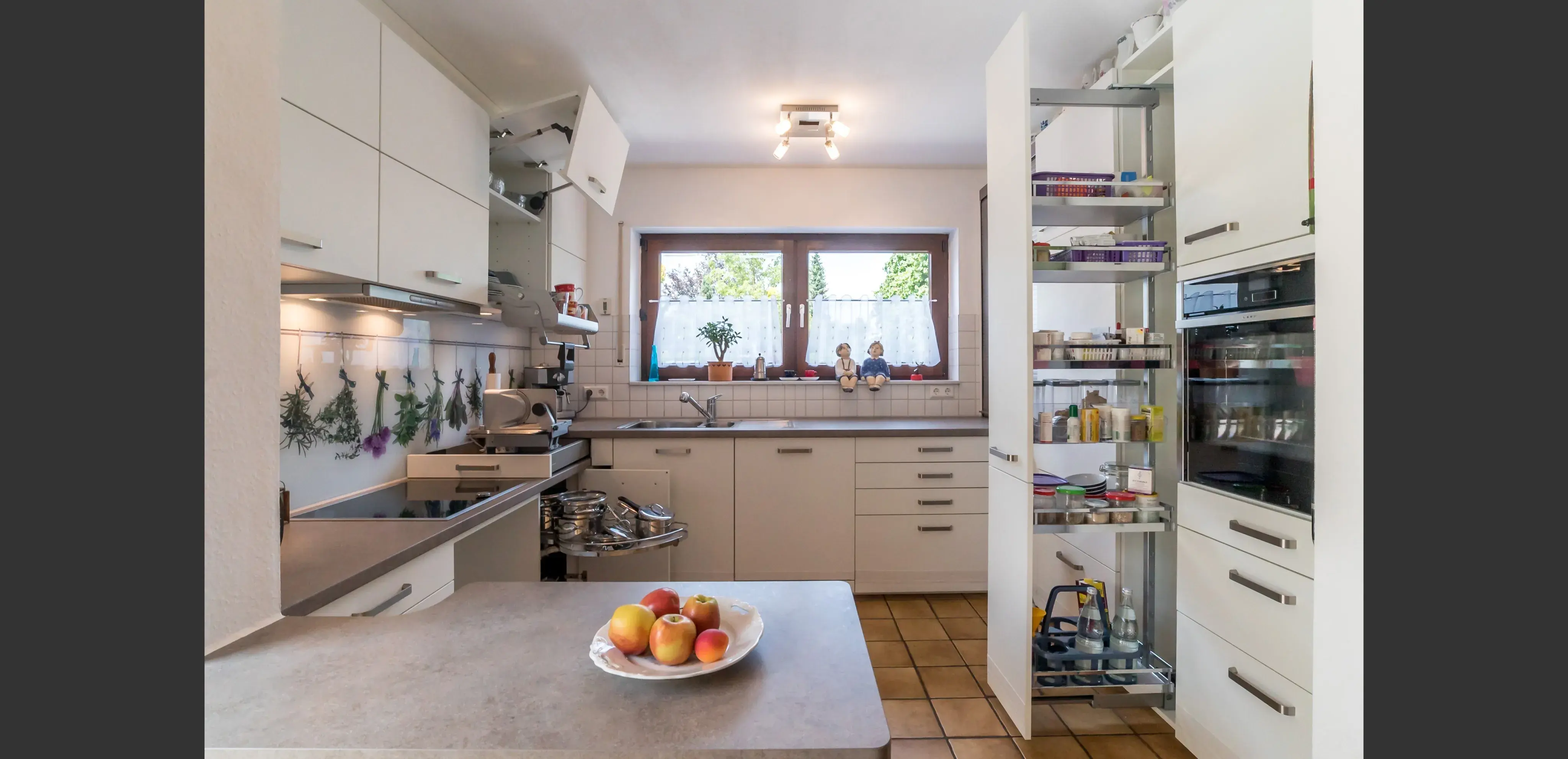 Moderne Küche mit weißen Schränken, offenem Vorratsschrank und Obstschale auf der Theke.