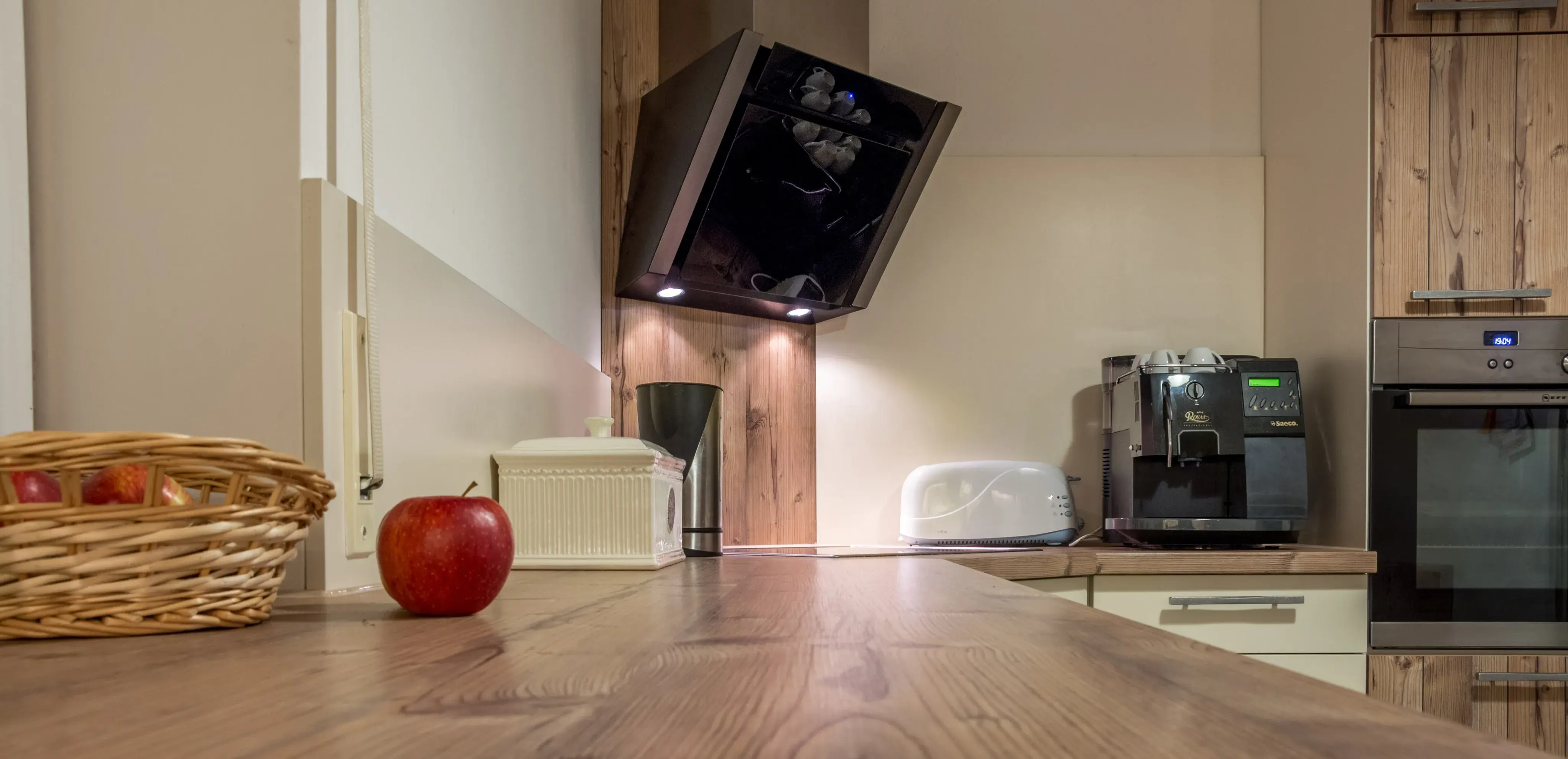 Moderne Küche mit Holzarbeitsplatte, rotem Apfel, Kaffeemaschine und Backofen.