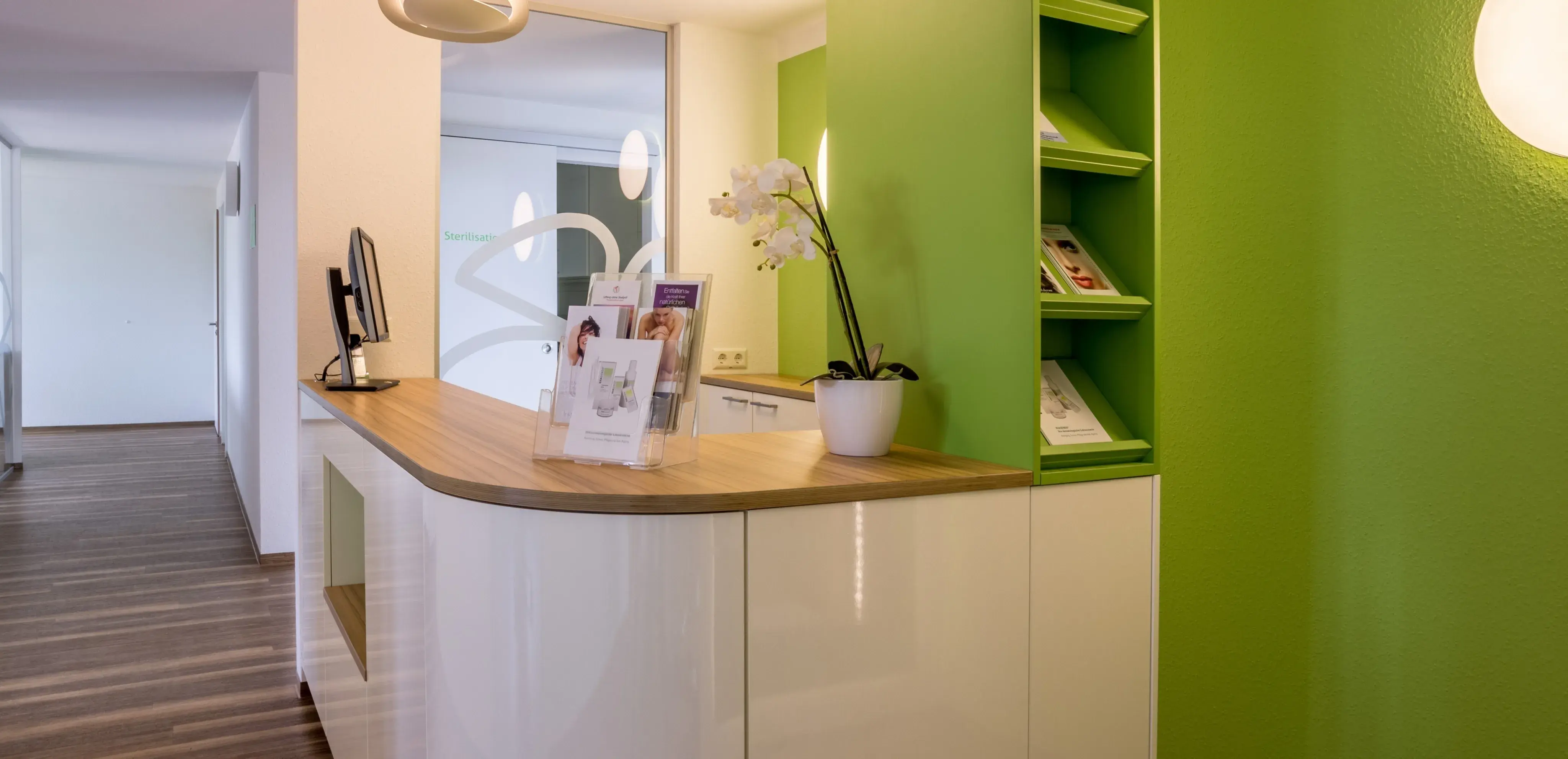 Moderne Empfangstheke mit grüner Wand, Holzplatte und weißem Orchideentopf.