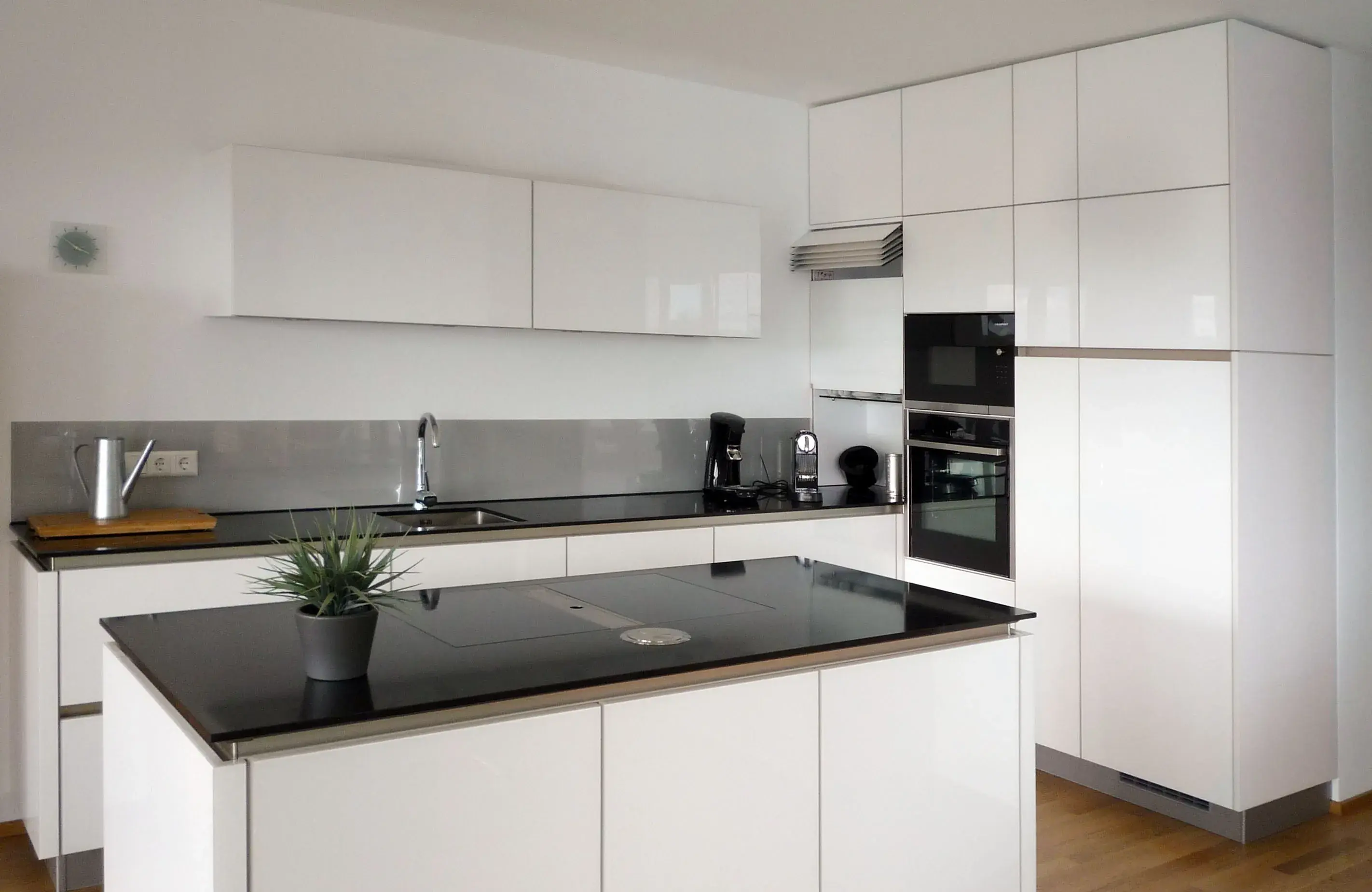 Moderne weiße Küche mit Kochinsel und schwarzer Arbeitsplatte.