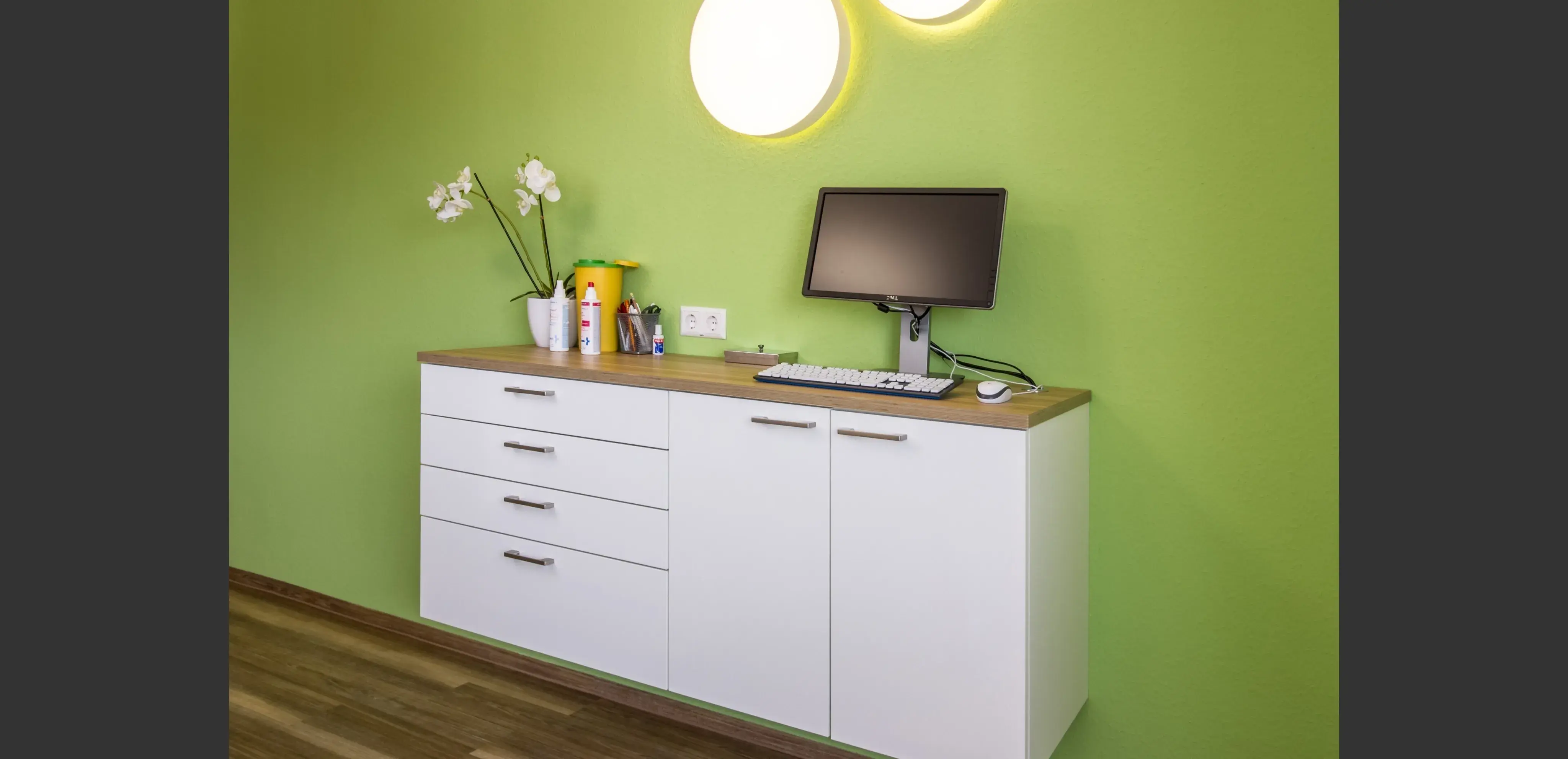 Weiße Kommode mit Monitor, Tastatur, Pflanzen und Deko vor grüner Wand
