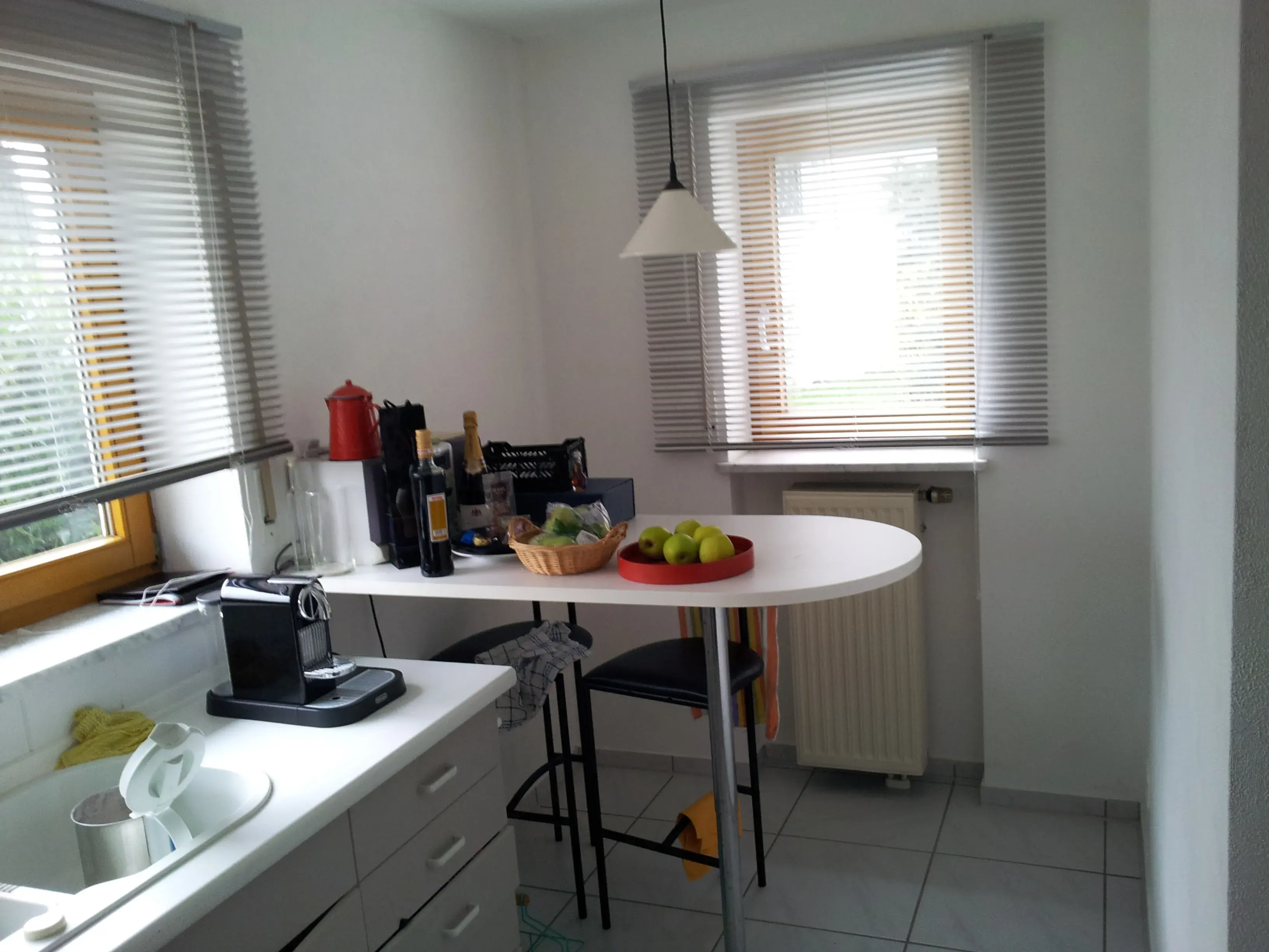 Helle Küche mit kleinem Tisch, Obstschale und Kaffeemaschine am Fenster.