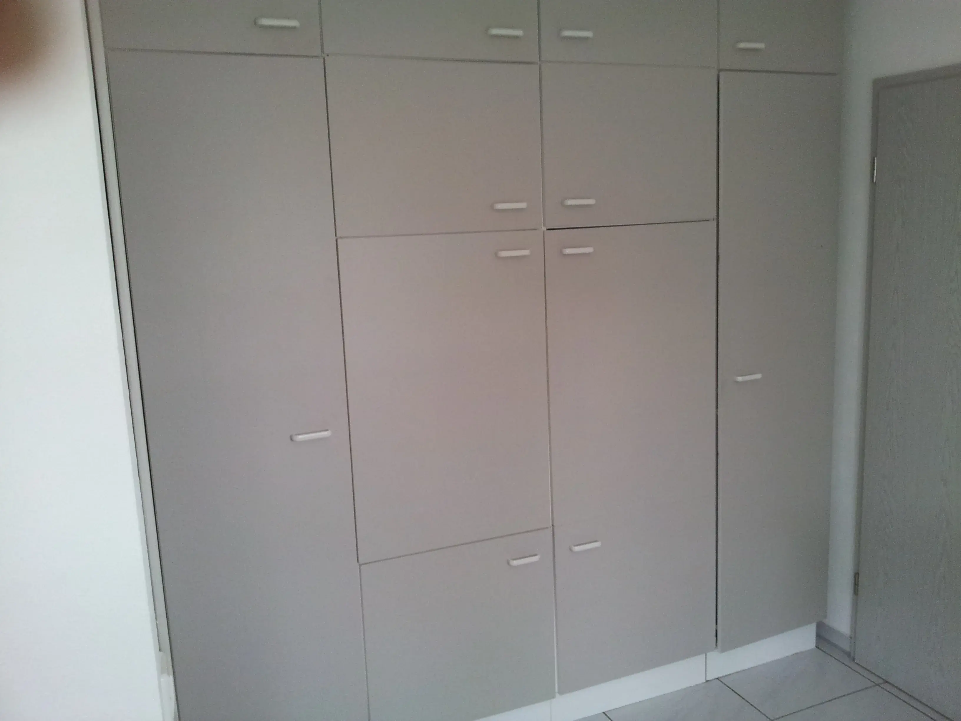 Großer, grauer Einbauschrank mit mehreren Schranktüren in einem hellen Raum.