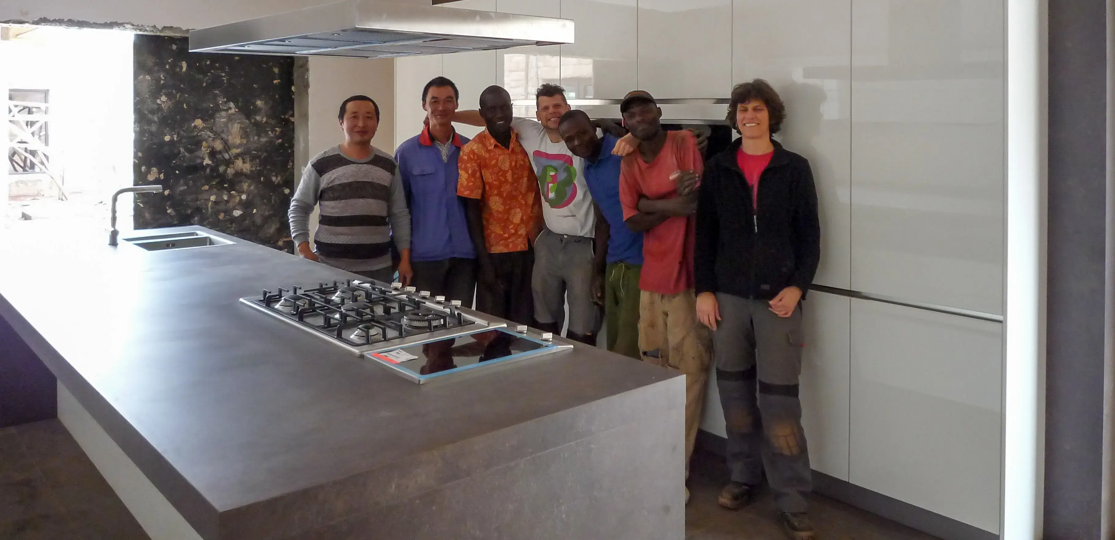 Sechs Menschen stehen in moderner Küche neben Kochinsel und lächeln.