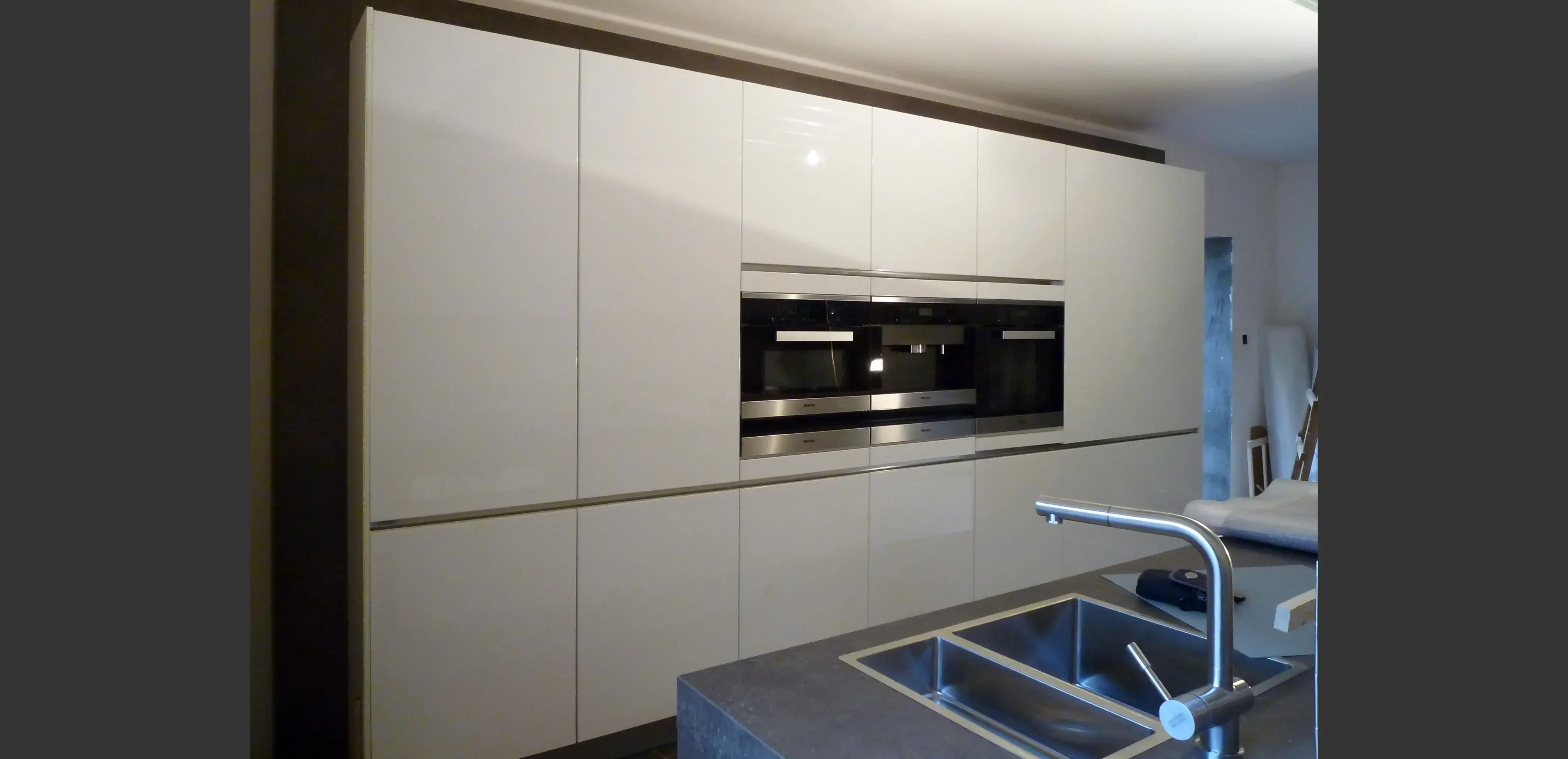 Moderne Küche mit weißen Hochglanzschränken, Einbauofen und Edelstahlspüle.