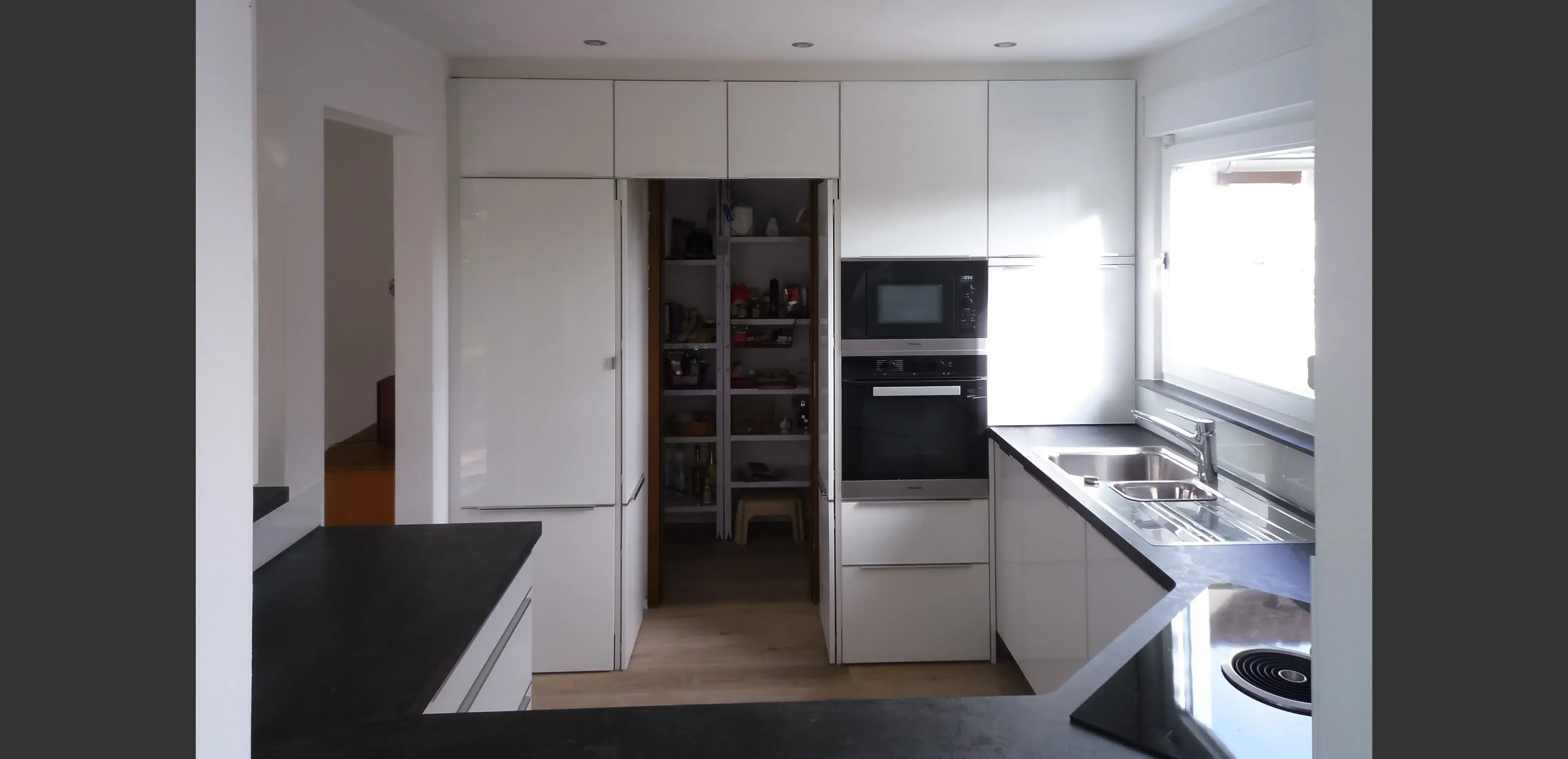 Moderne weiße Küche mit offenem Vorratsraum und viel Tageslicht.