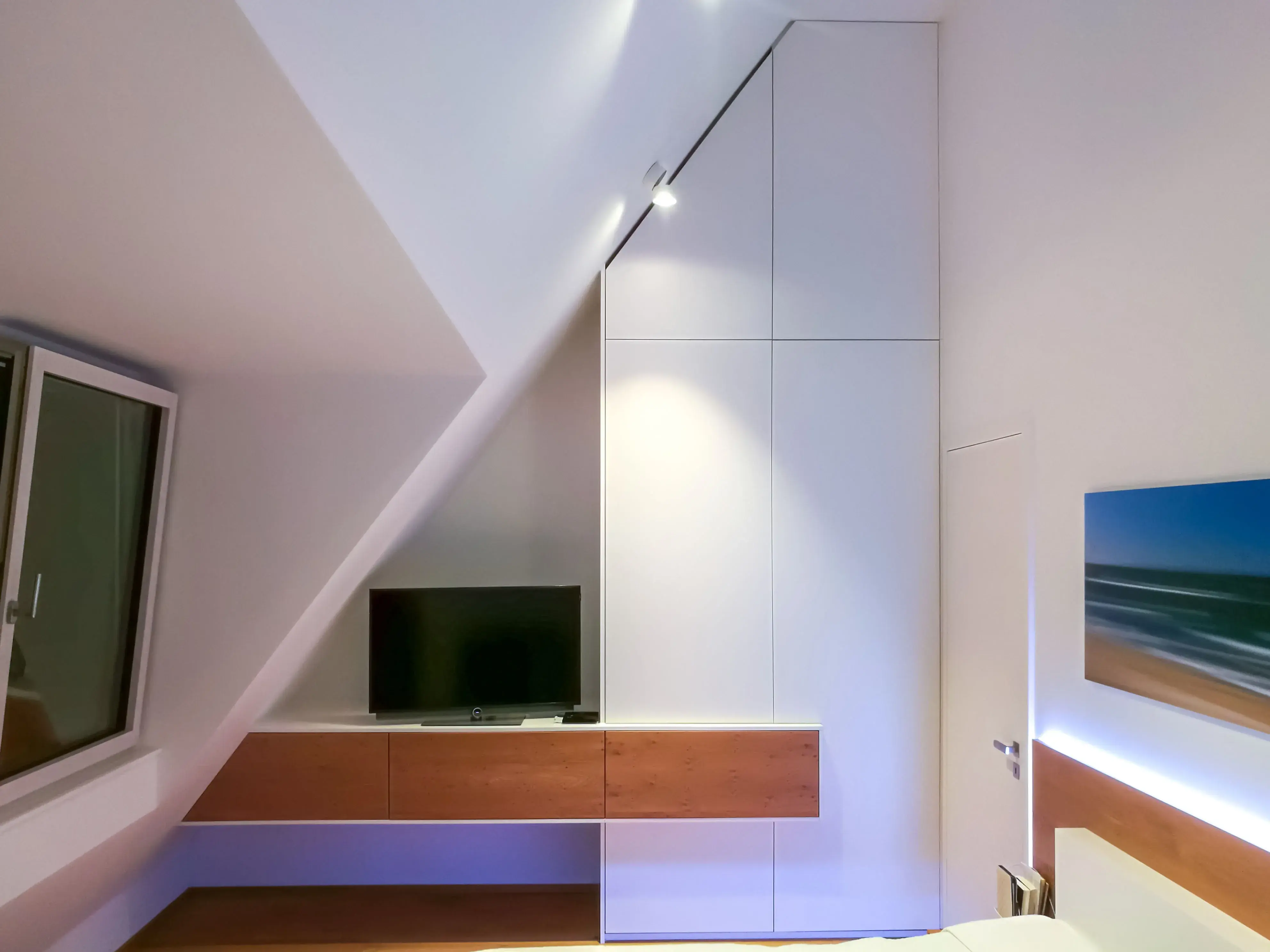 Modernes Schlafzimmer mit schräger Decke, TV, Fenster und Wandbild.