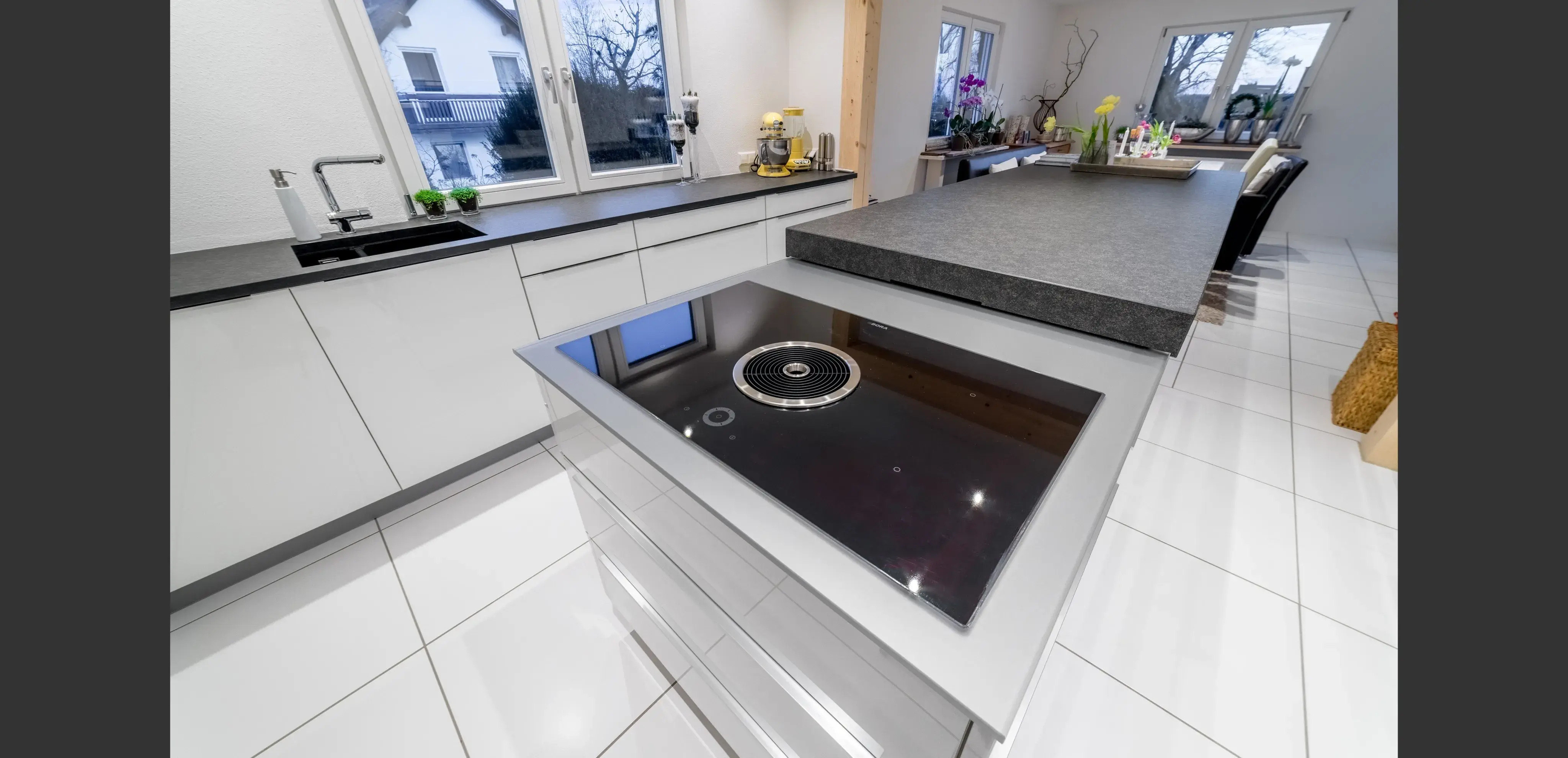 Moderne, helle Küche mit Kochinsel und Induktionskochfeld, große Fenster im Hintergrund