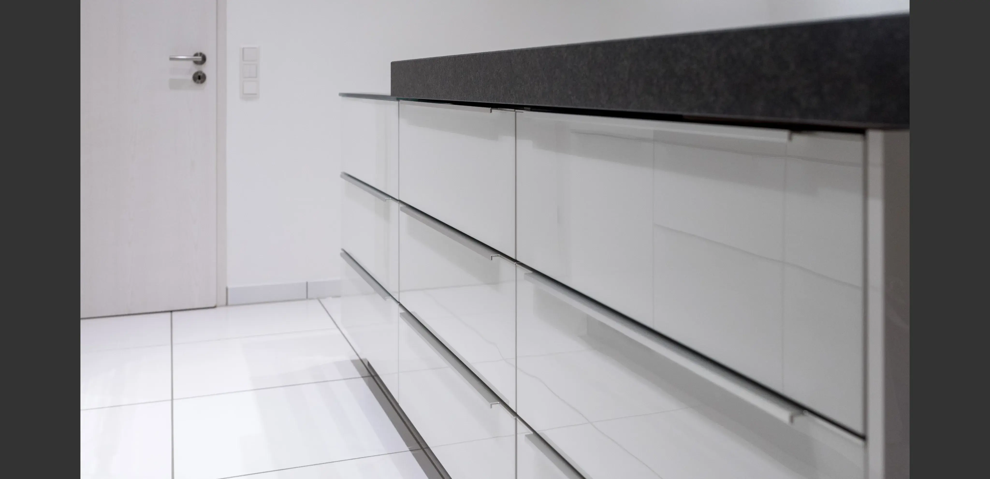 Moderne weiße Küchenschränke mit glänzender Oberfläche und dunkler Arbeitsplatte