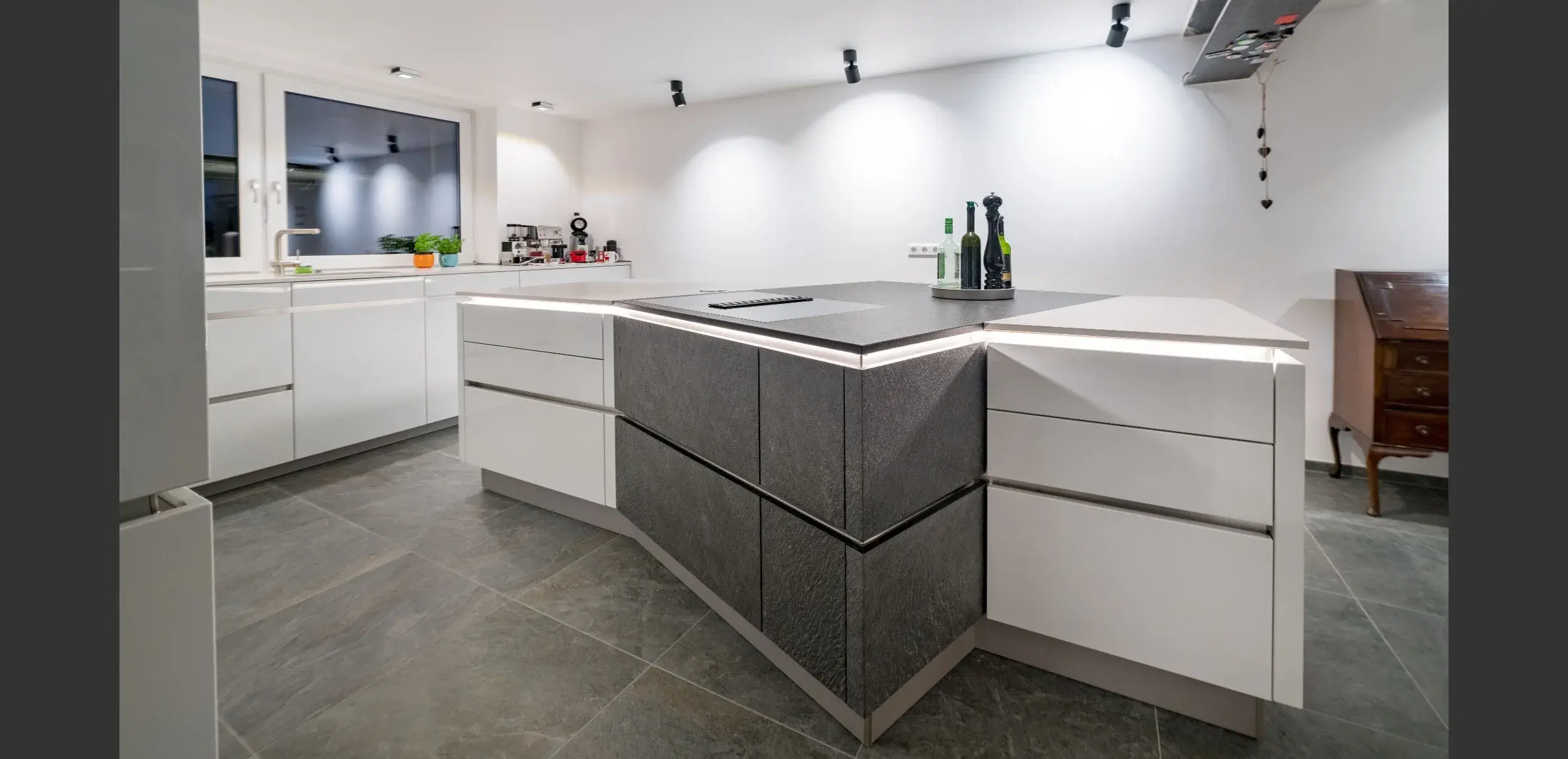 Moderne Küche mit weißem Interieur und grauer Kücheninsel, helle Beleuchtung.