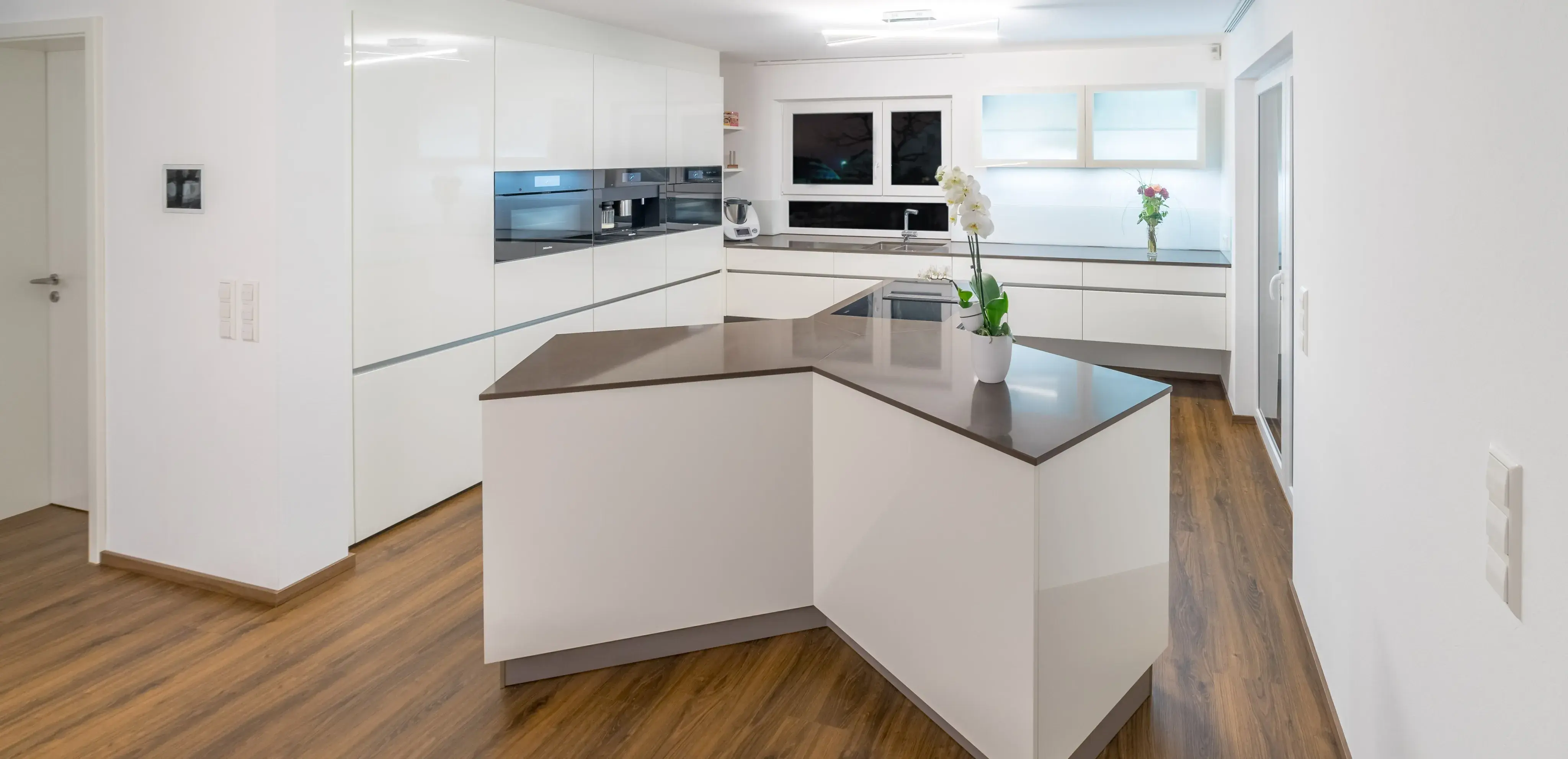 Moderne weiße Küche mit Holzboden und Kochinsel, Orchidee als Dekoration.