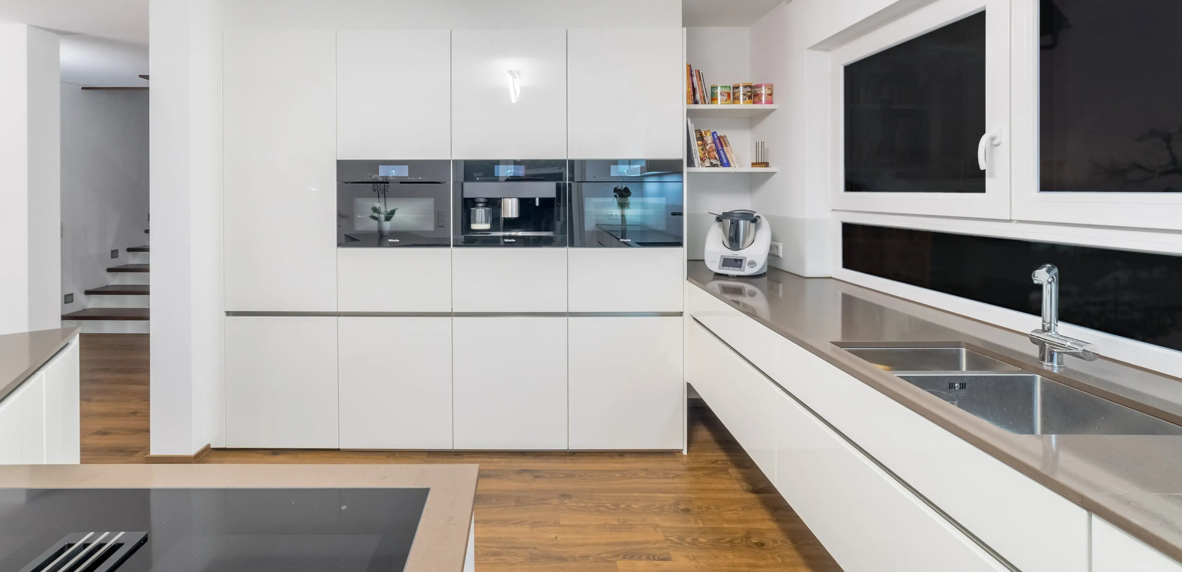 Moderne, helle Küche mit weißen Schränken, Edelstahlgeräten und großem Fenster.