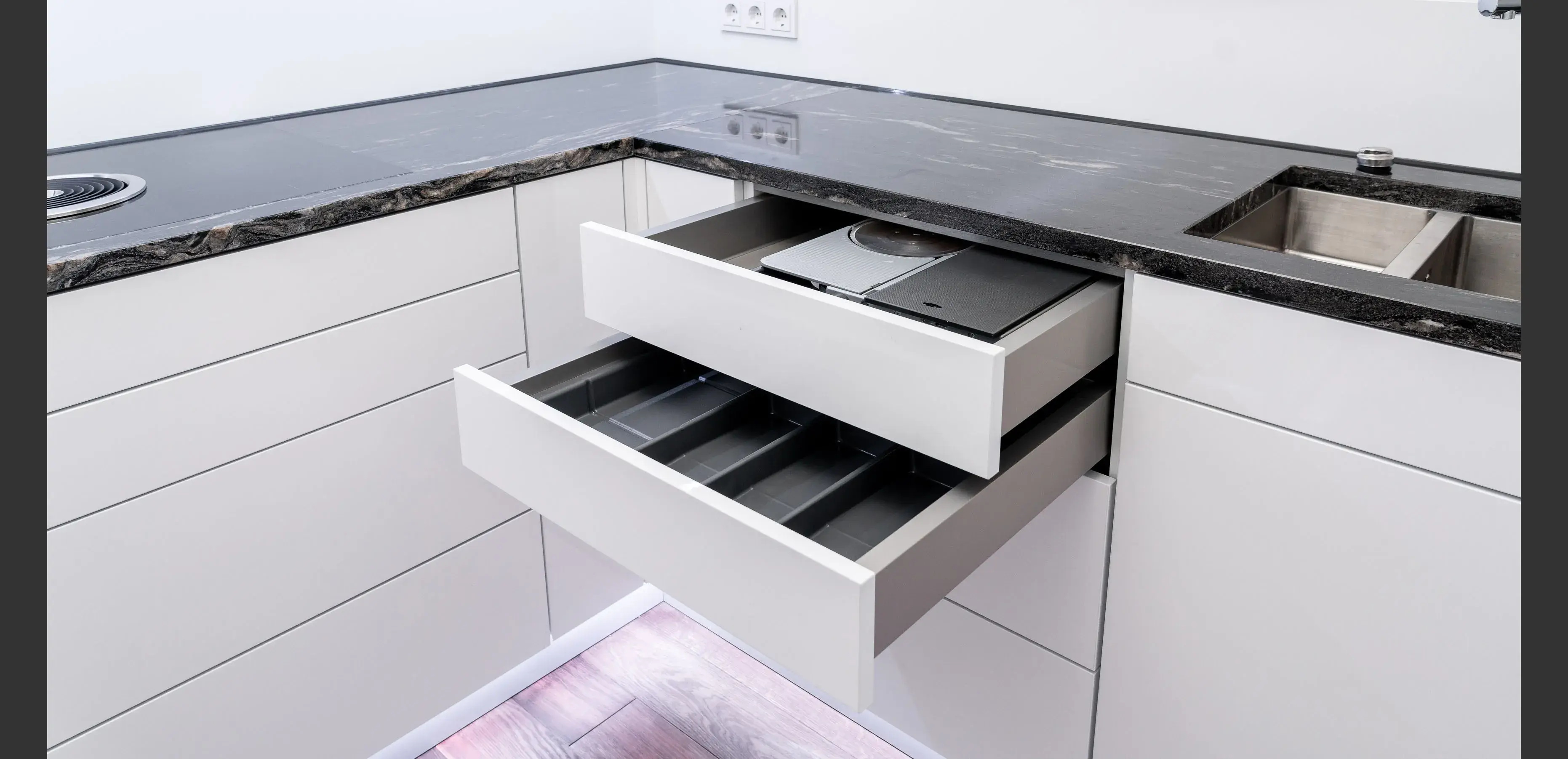 Zwei ausgezogene Küchenschubladen mit Besteckfächern unter schwarzer Arbeitsplatte.