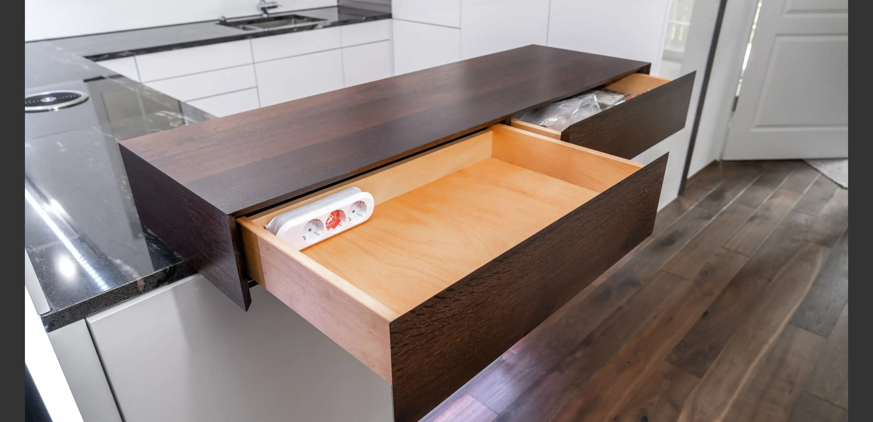 Offene Küchenschublade aus Holz mit Folienrolle, moderner Boden und weiße Möbel.