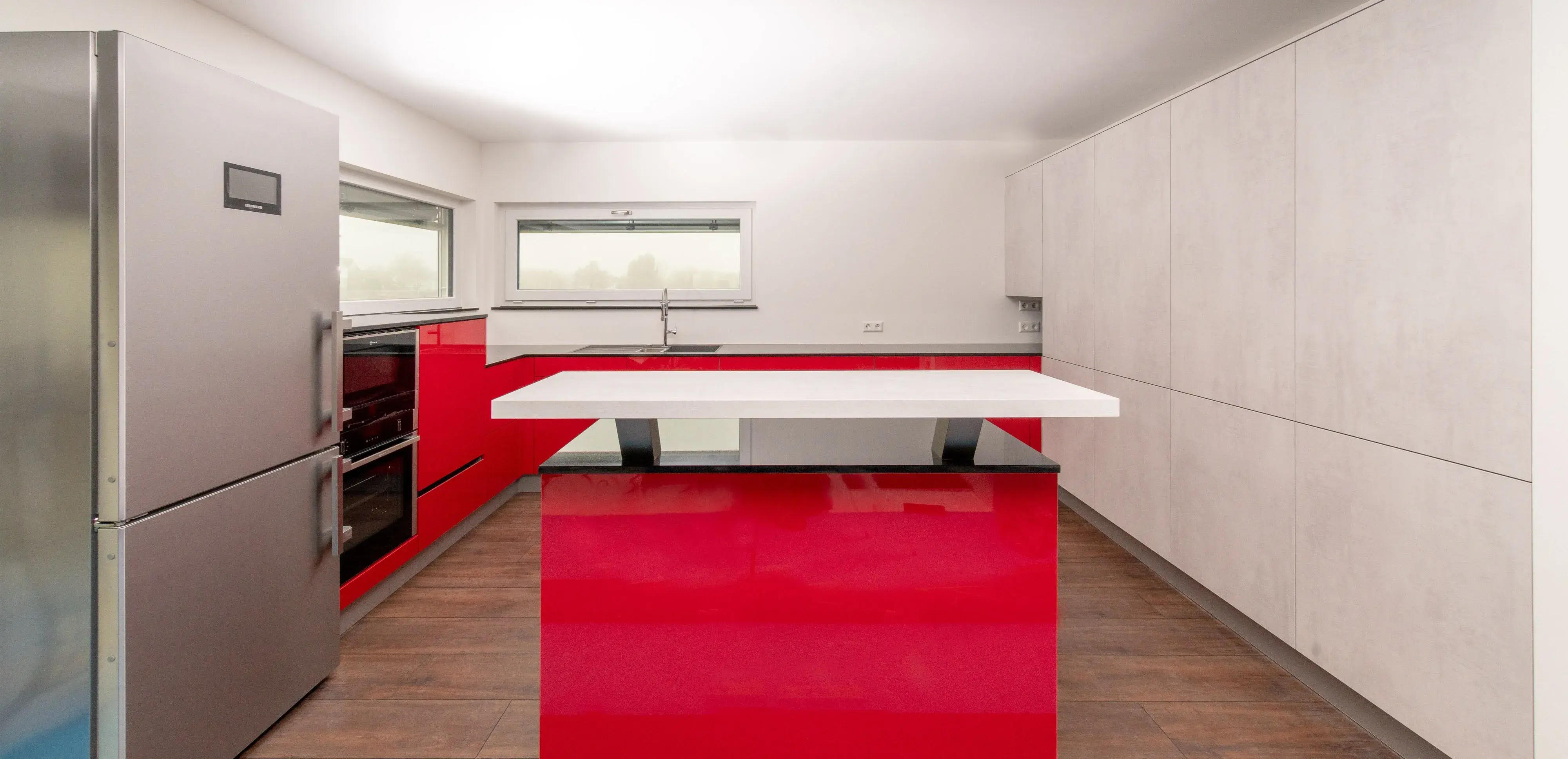 Moderne Küche mit roten Schränken, Kücheninsel und Edelstahlkühlschrank.