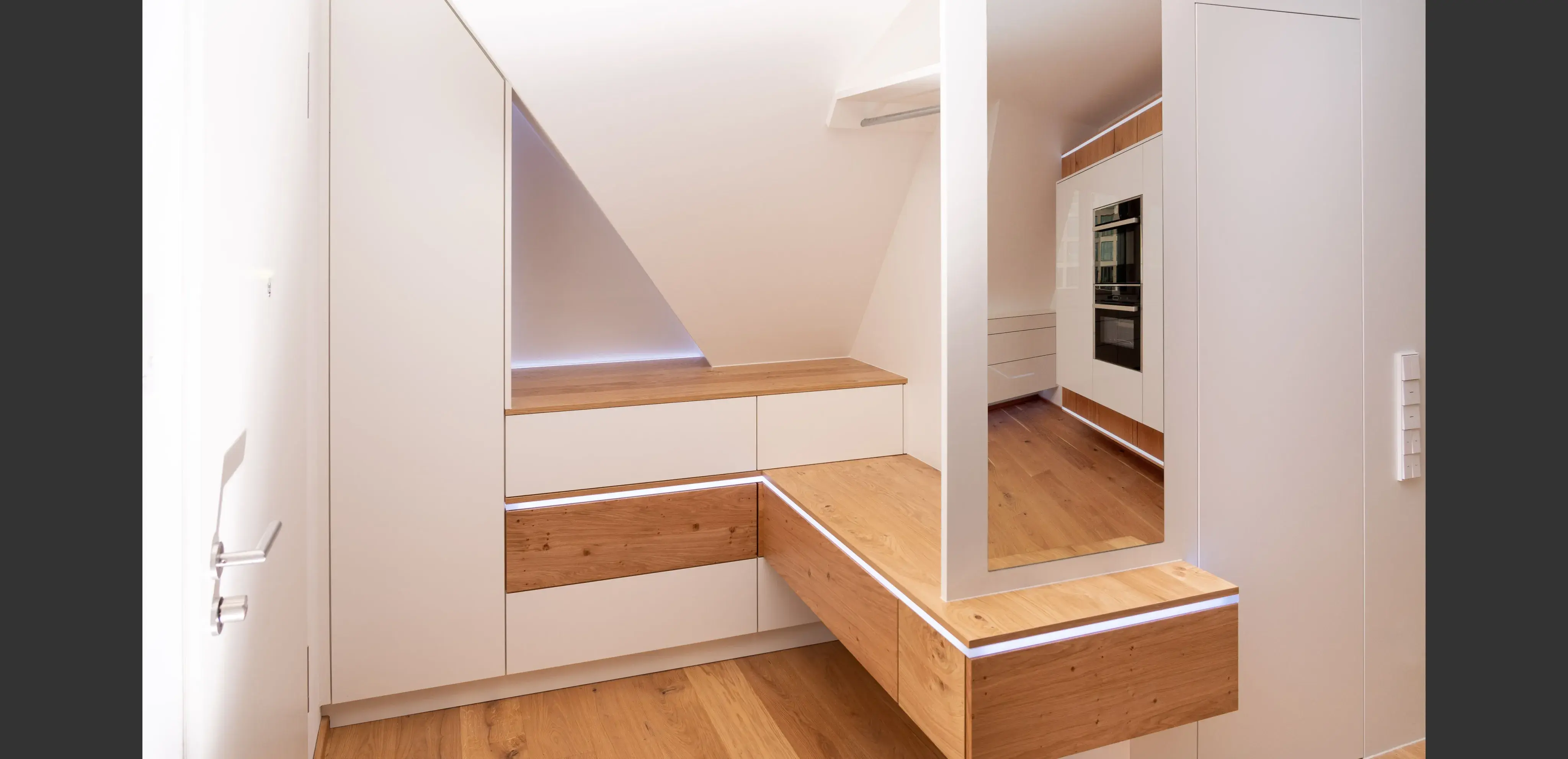 Heller Ankleidezimmer mit weißen Schränken, Holzflächen und großem Spiegel.