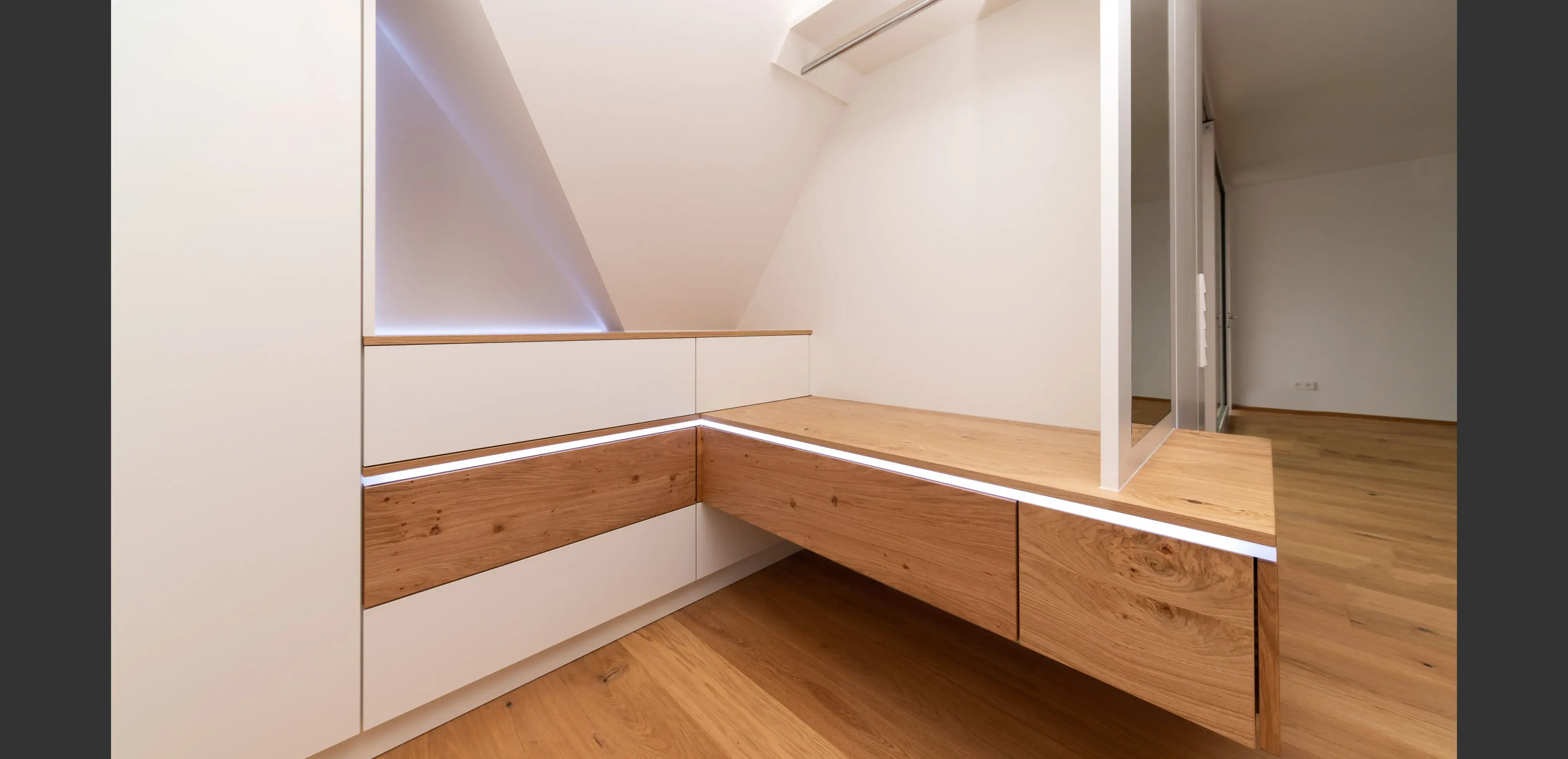 Modernes Ankleidezimmer mit Holz- und weißen Schubladen, Spiegel und Parkettboden.