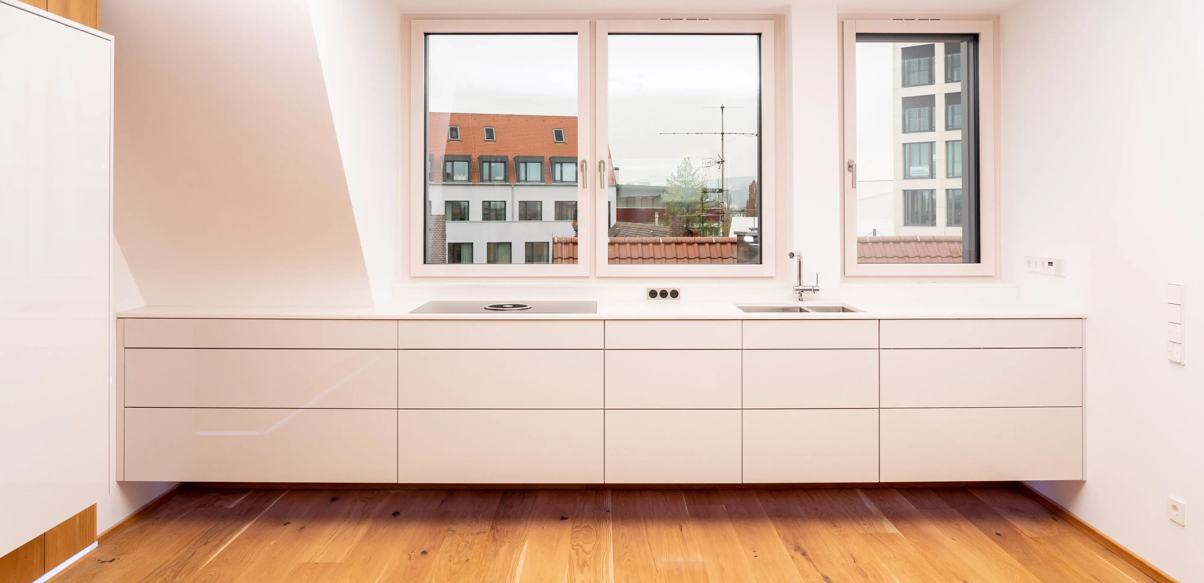 Moderne, minimalistische Küche mit weißen Schränken und Holzboden, drei große Fenster.