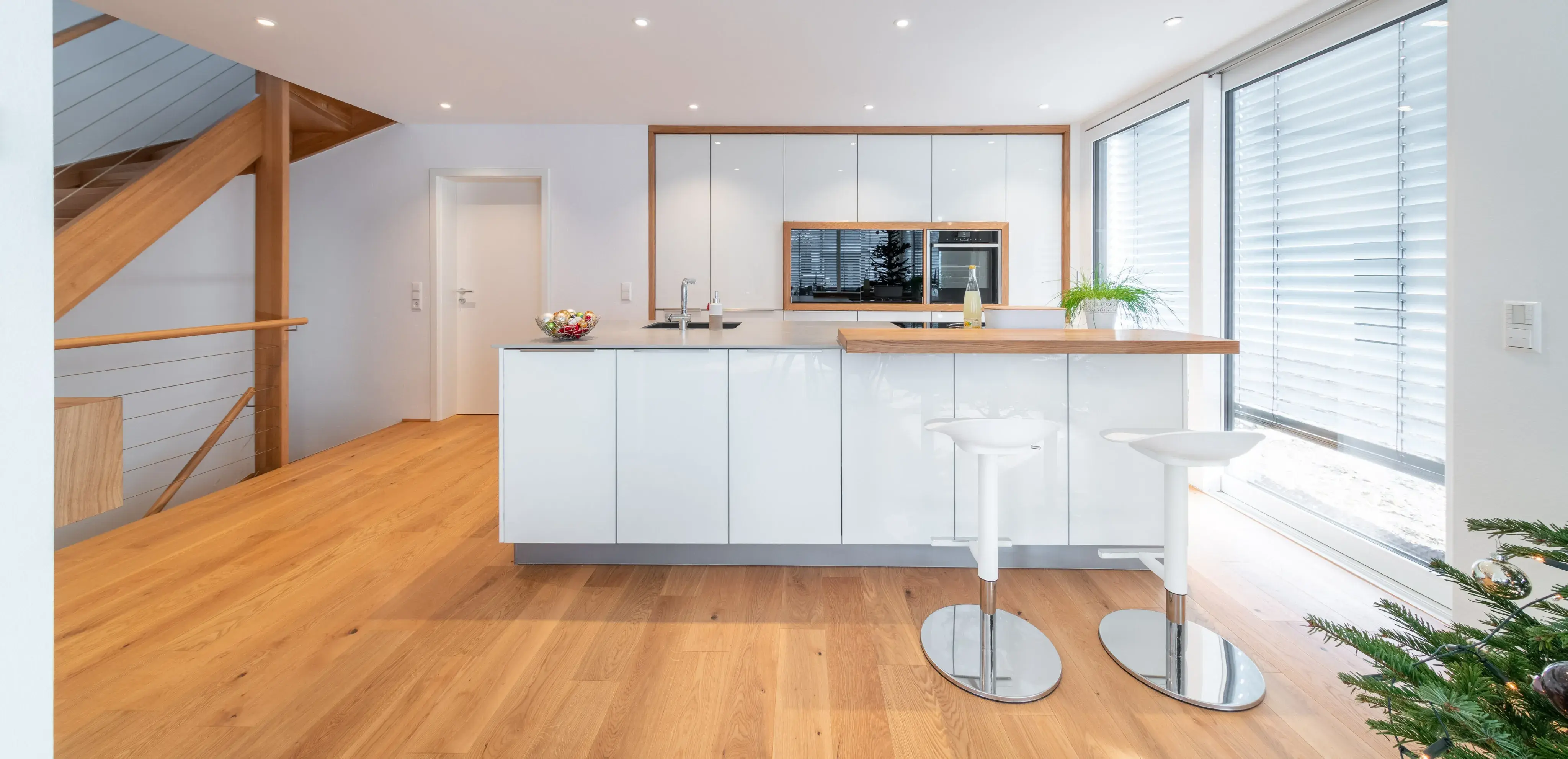 Moderne, helle Küche mit Kochinsel, Holzfußboden und großen Fenstern mit Jalousien.