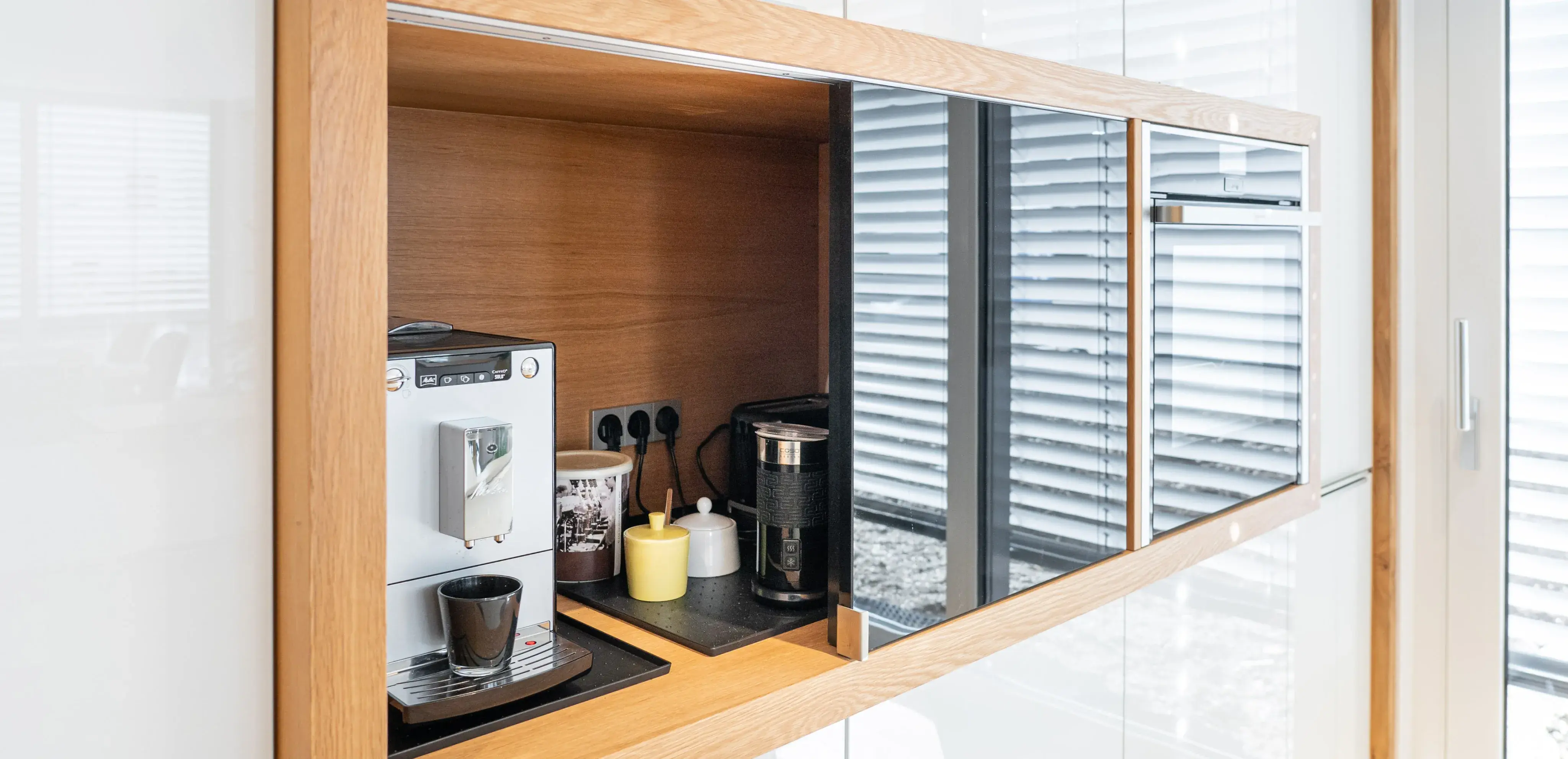 Kaffee-Ecke mit Espressomaschine, Kaffeepadmaschine und Tassen in modernem Holzregal.