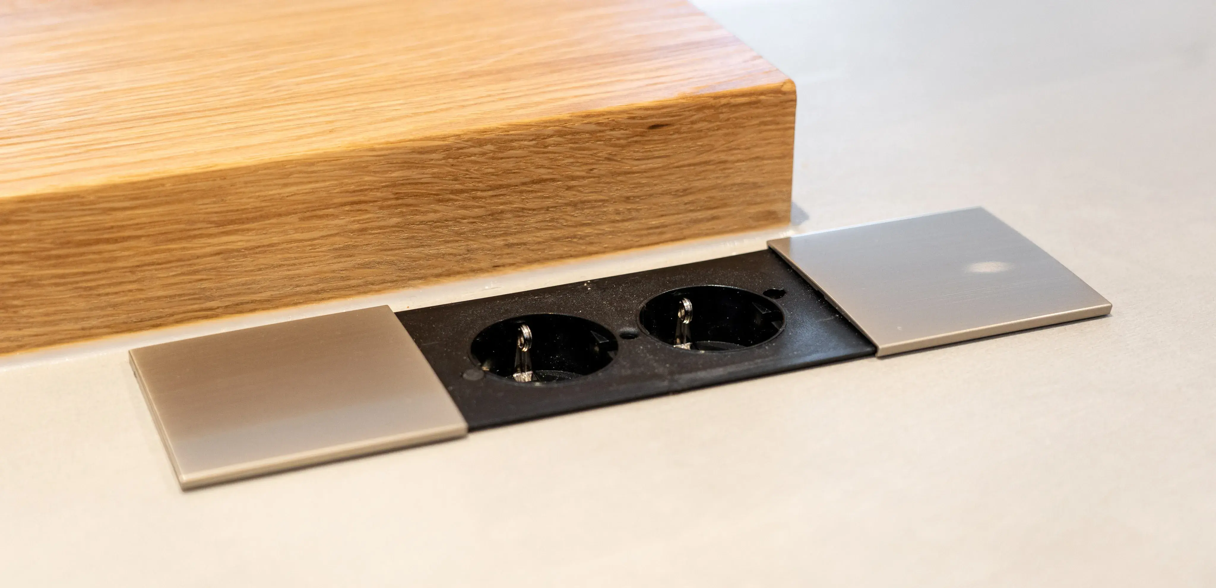 Zwei schwarze Steckdosen in einer modernen, eingelassenen Abdeckung neben Holzoberfläche.