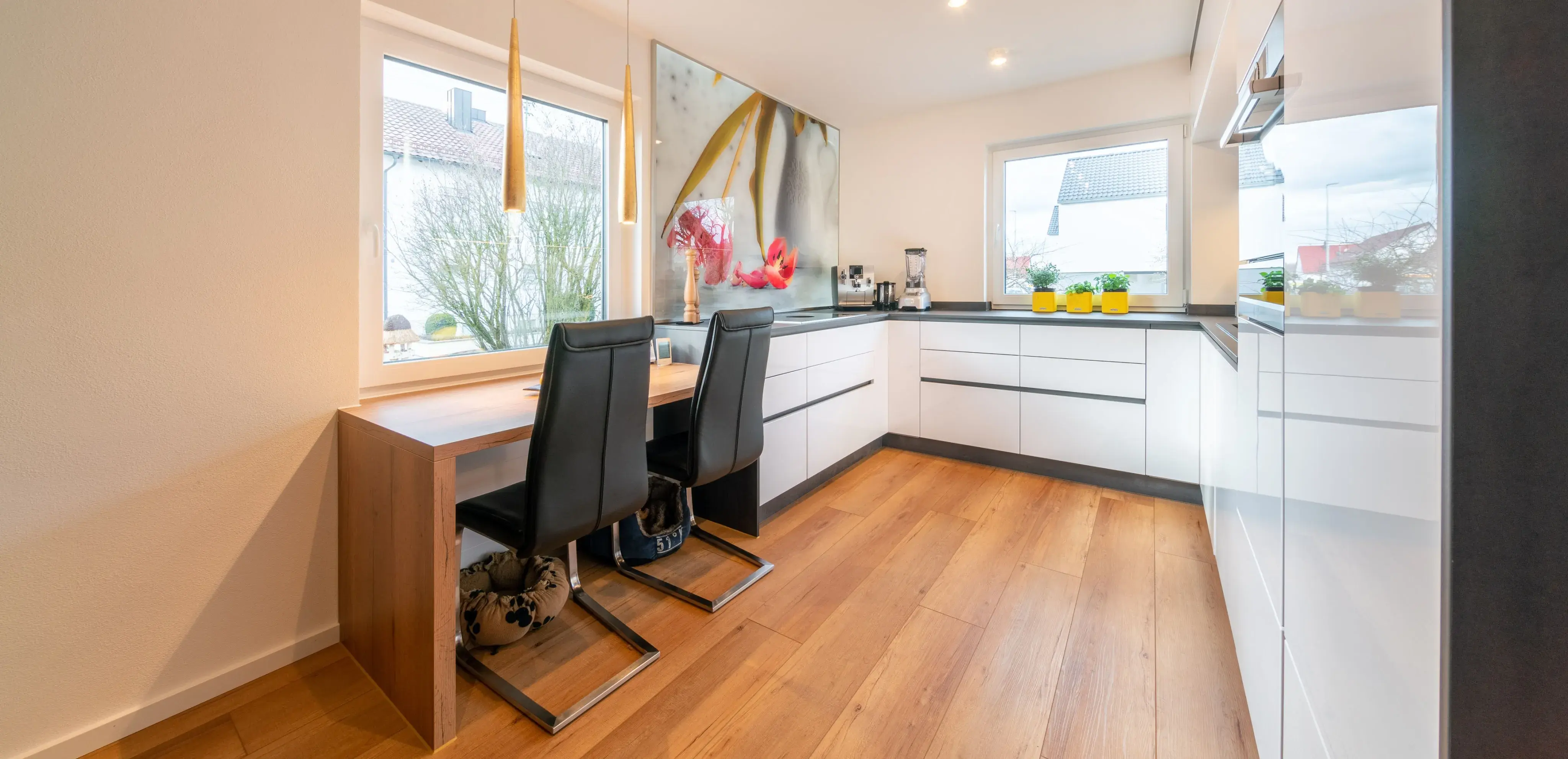 Moderne weiße Küche mit Holzfußboden, Esstisch und großen Fenstern.