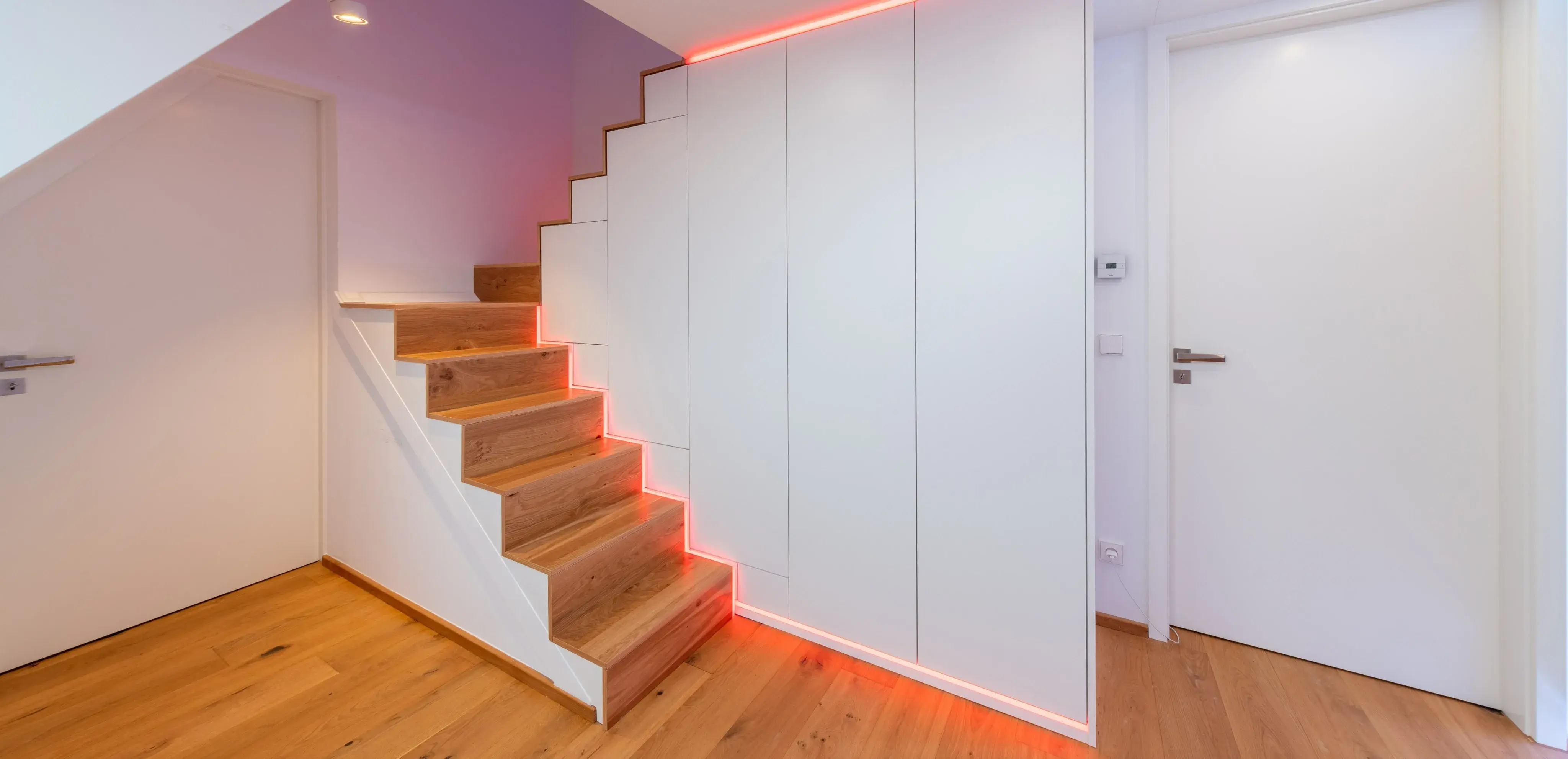 Holztreppe mit roter LED-Beleuchtung an der Wand in modernem Flur