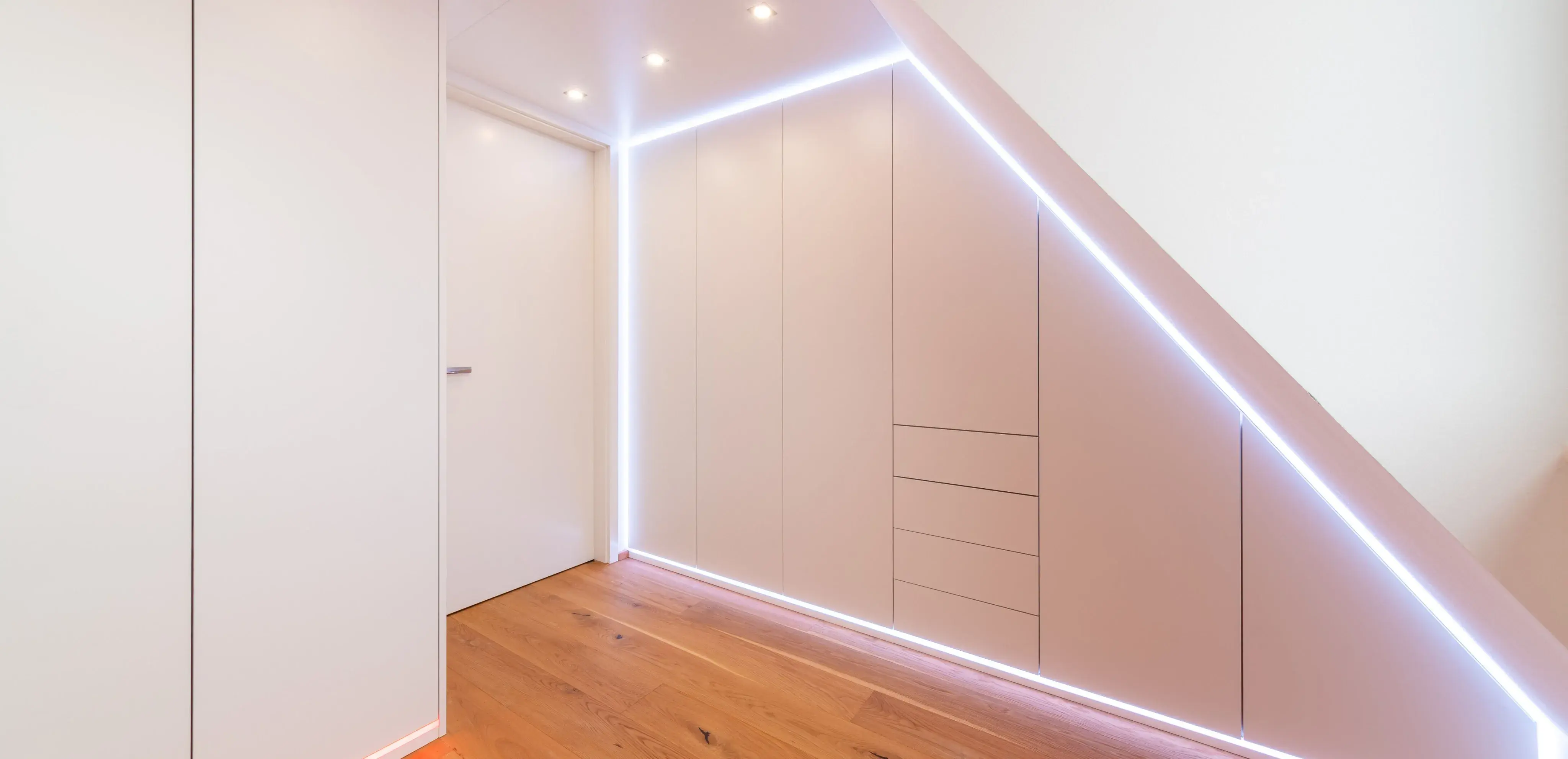 Moderner Einbauschrank unter Dachschräge mit LED-Beleuchtung und Holzfußboden.
