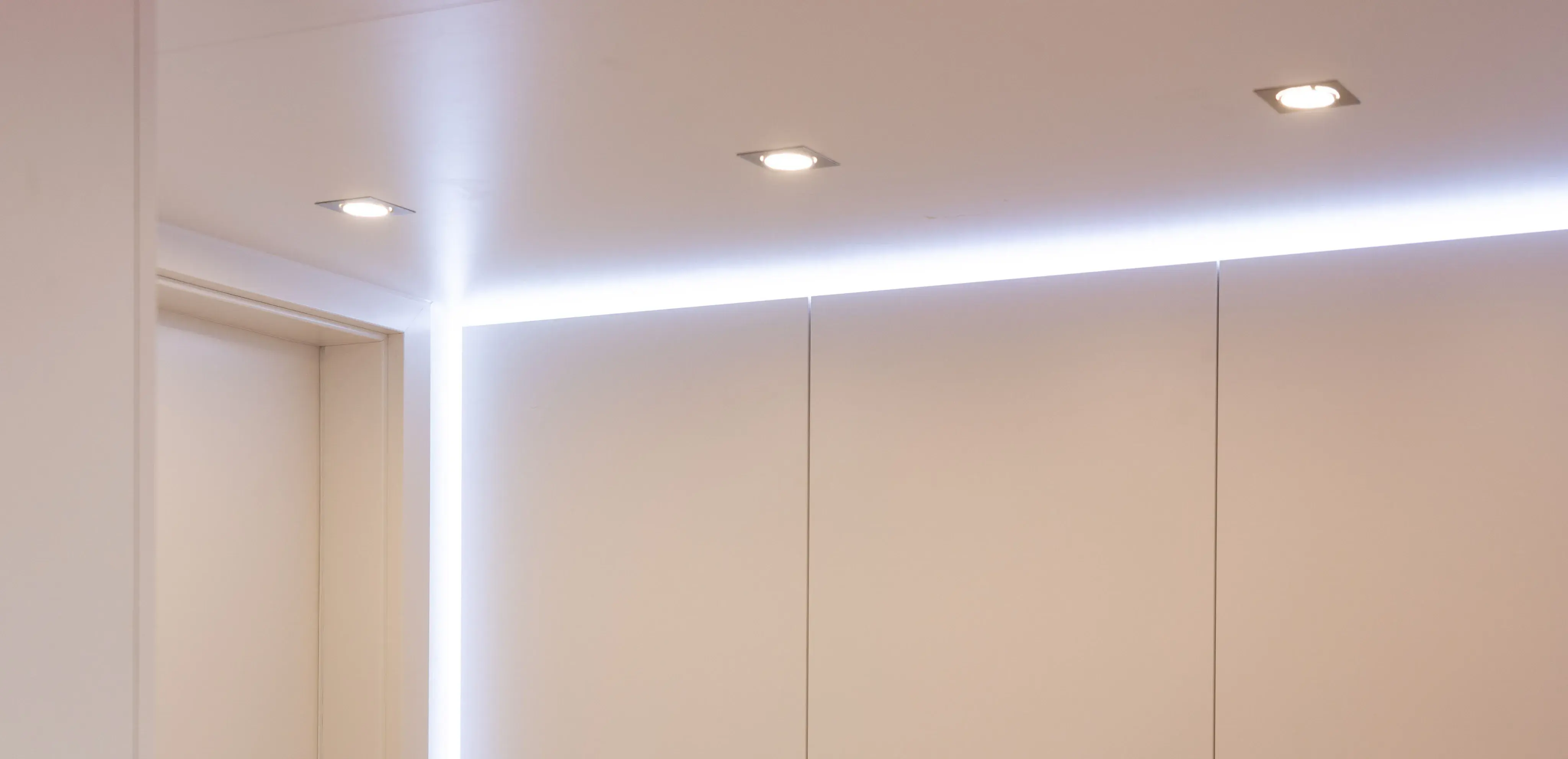 Weißer Raum mit LED-Lichtleiste an Wand und Decke, drei eingelassene Deckenstrahler