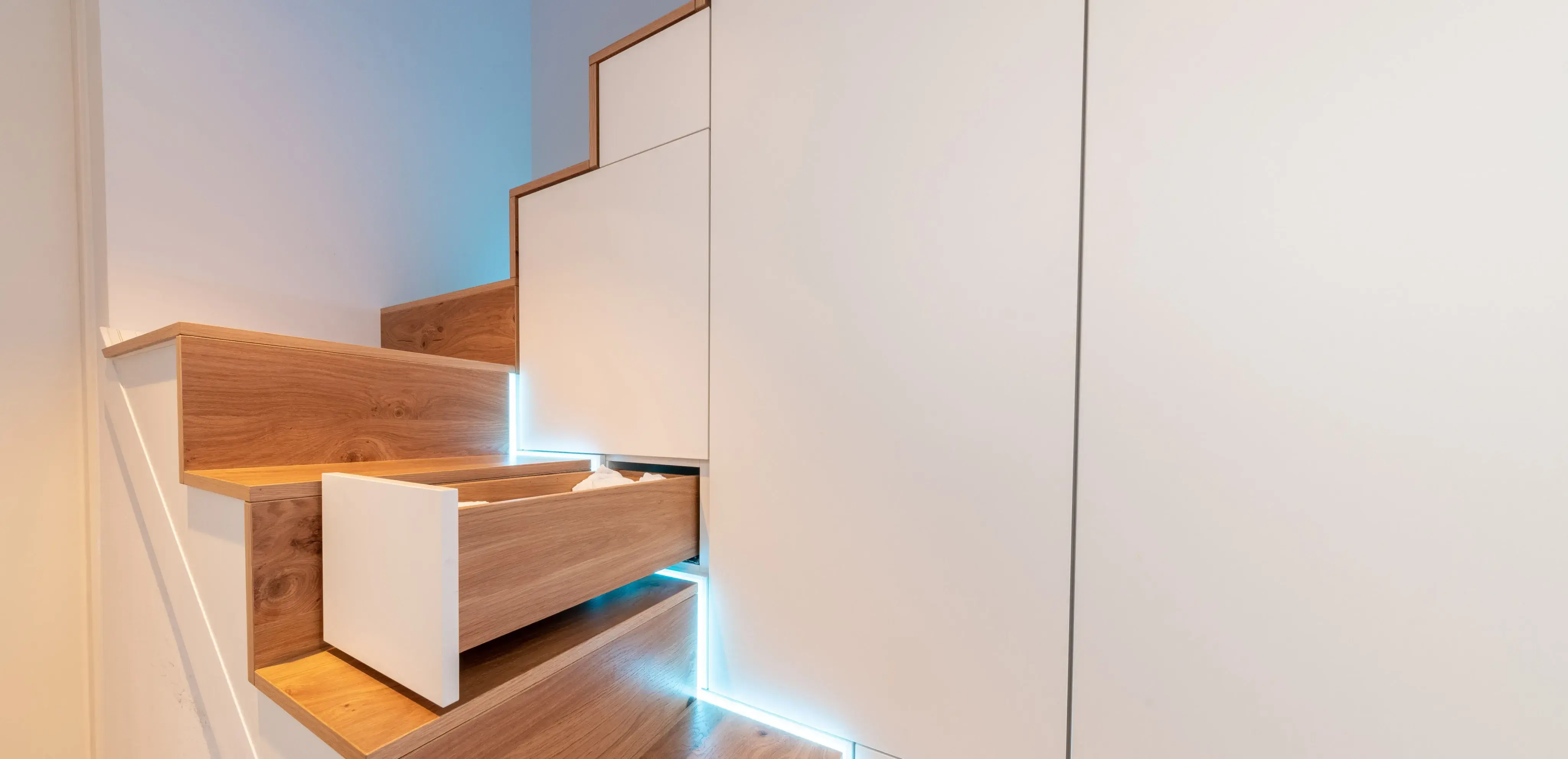 Holztreppe mit Schubladen im Stufen, indirektes blaues Licht.