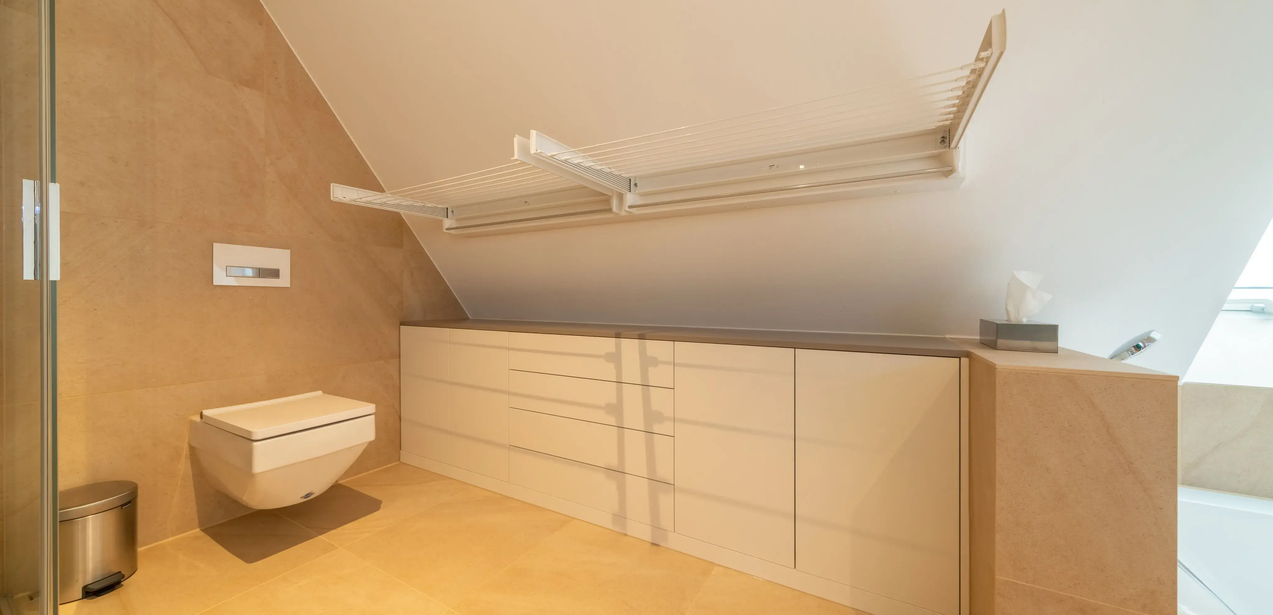 Modernes Badezimmer mit Wandtoilette, Dachschräge und weißem Schrank unter Trockenstangen.