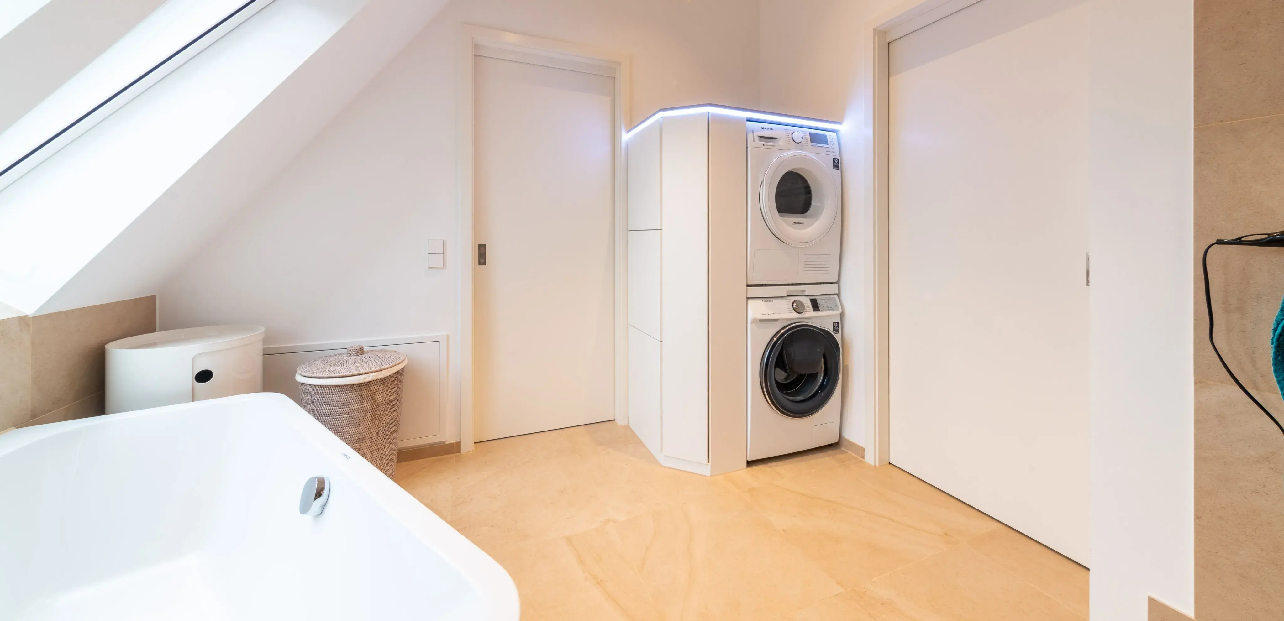 Helles Badezimmer mit Badewanne, WC und stapelbarer Waschmaschine und Trockner.