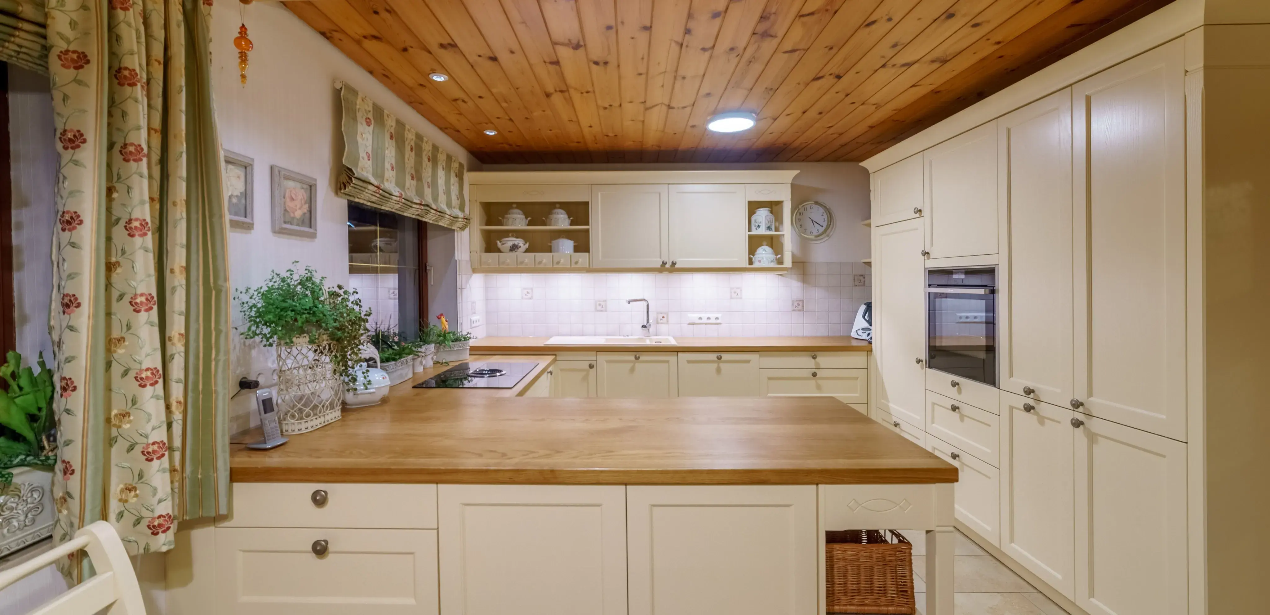 Helle Landhausküche mit Holzdecke, weißen Schränken und großen Arbeitsplatten.