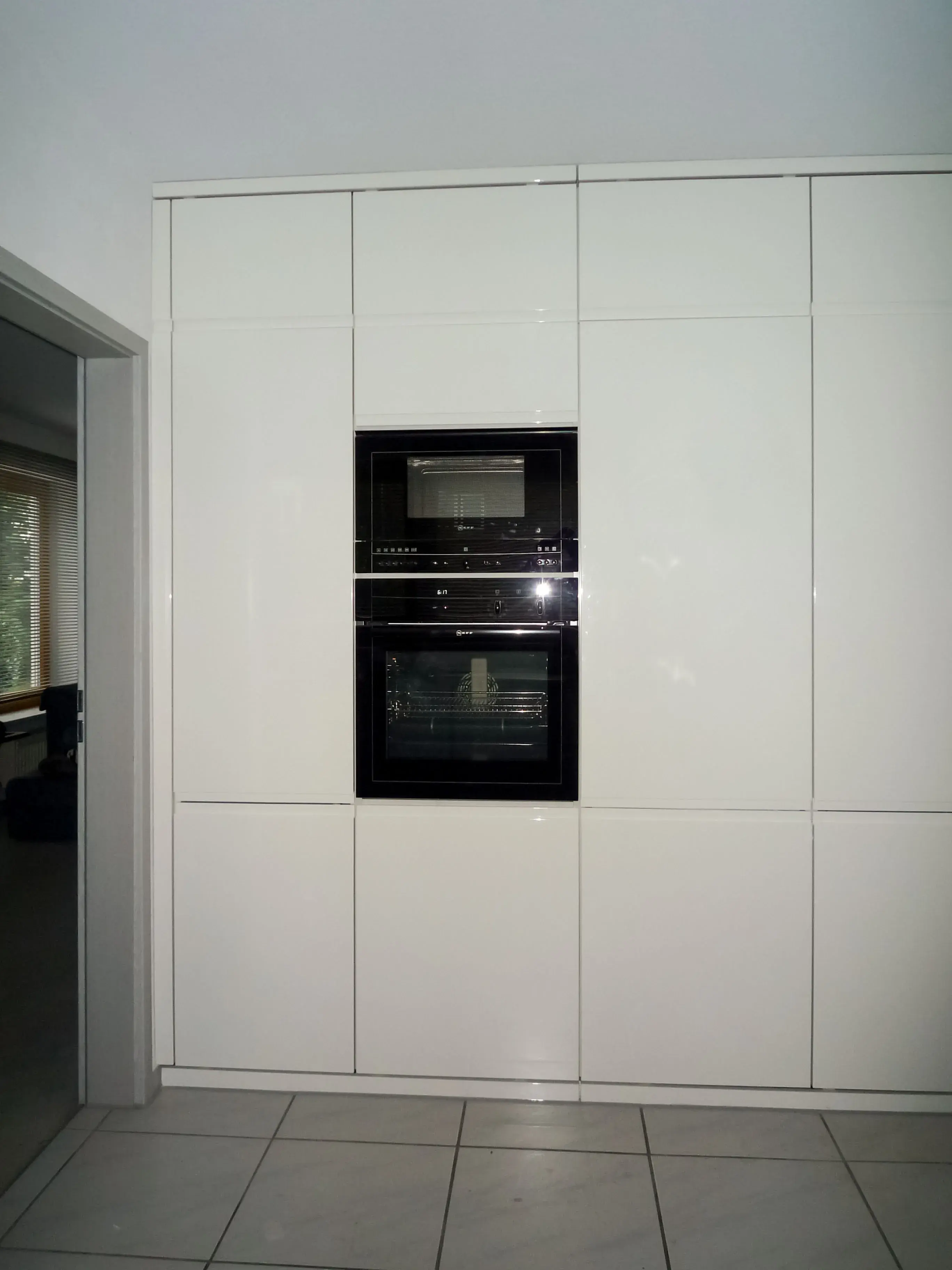 Moderne, weiße Einbauküche mit schwarzem Backofen und Mikrowelle in der Wand.