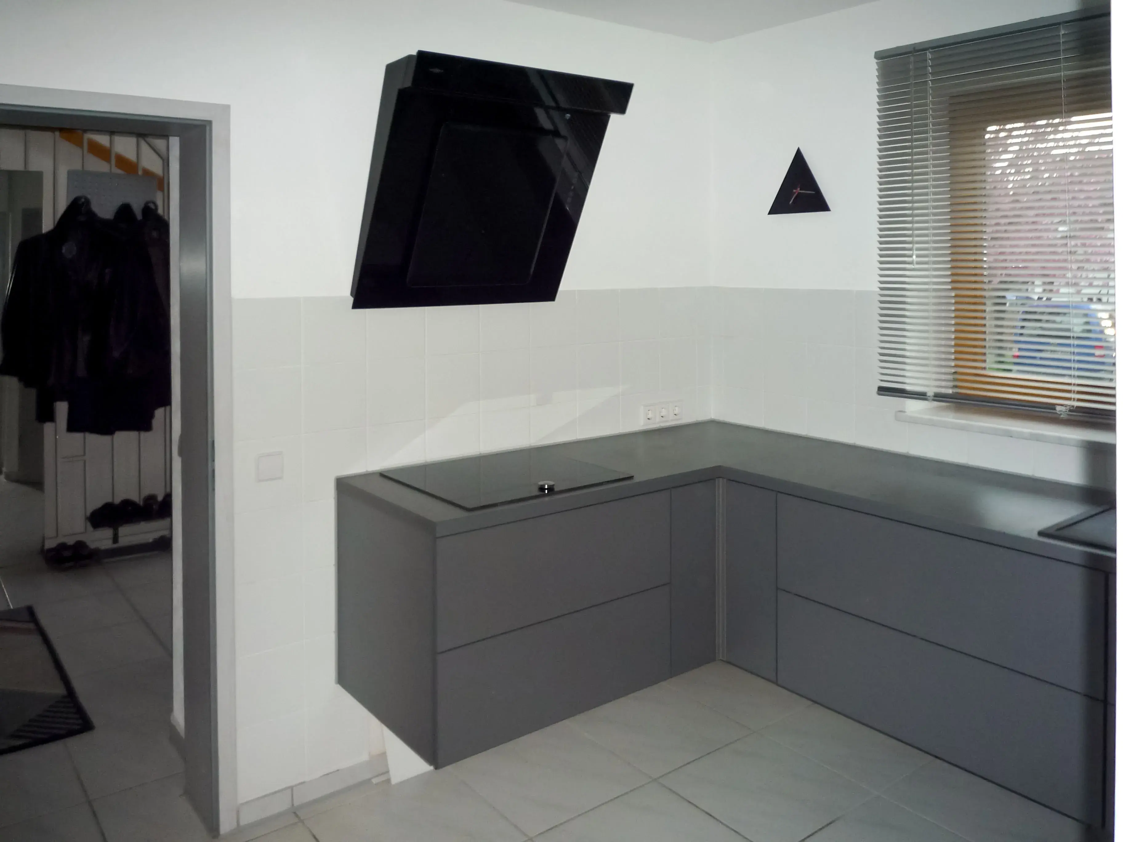 Moderne Küche mit grauen Schränken, schwarzer Dunstabzugshaube und Fenster.