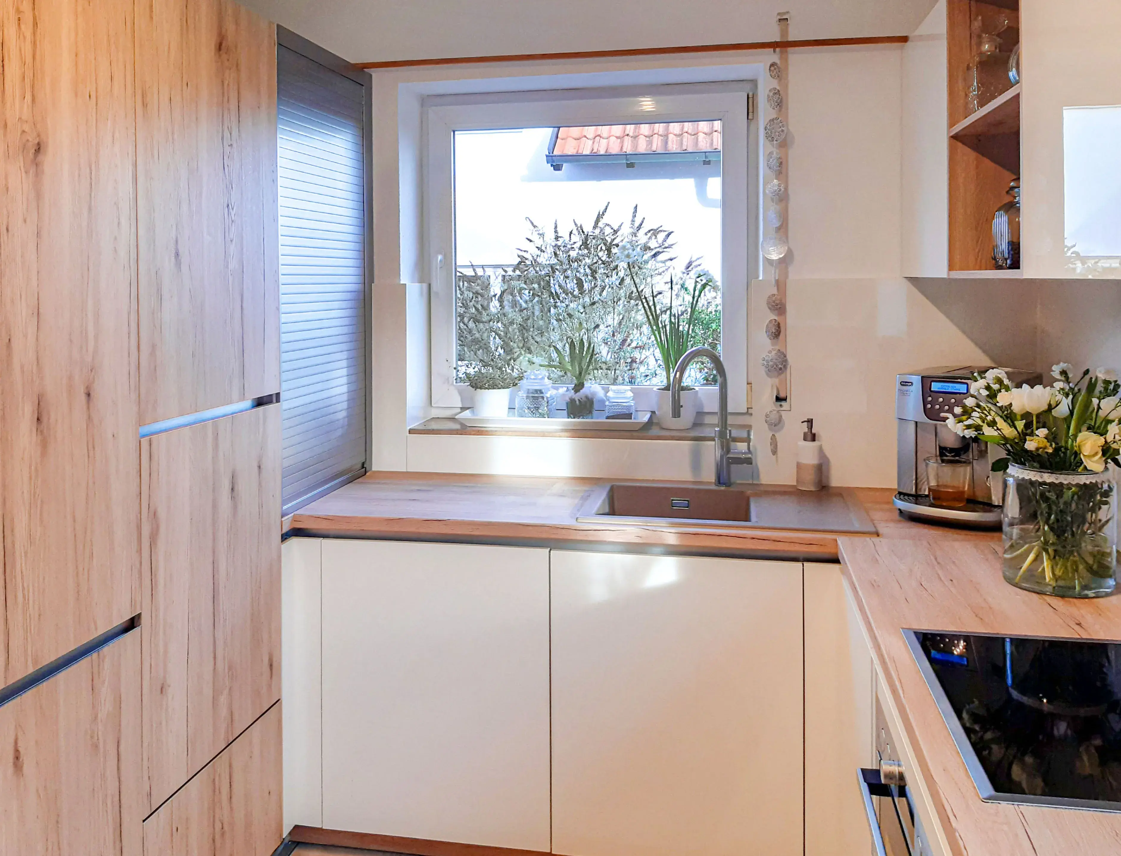 Moderne Küche mit Holzfronten, hellem Arbeitsbereich und Fenster mit Pflanzen.