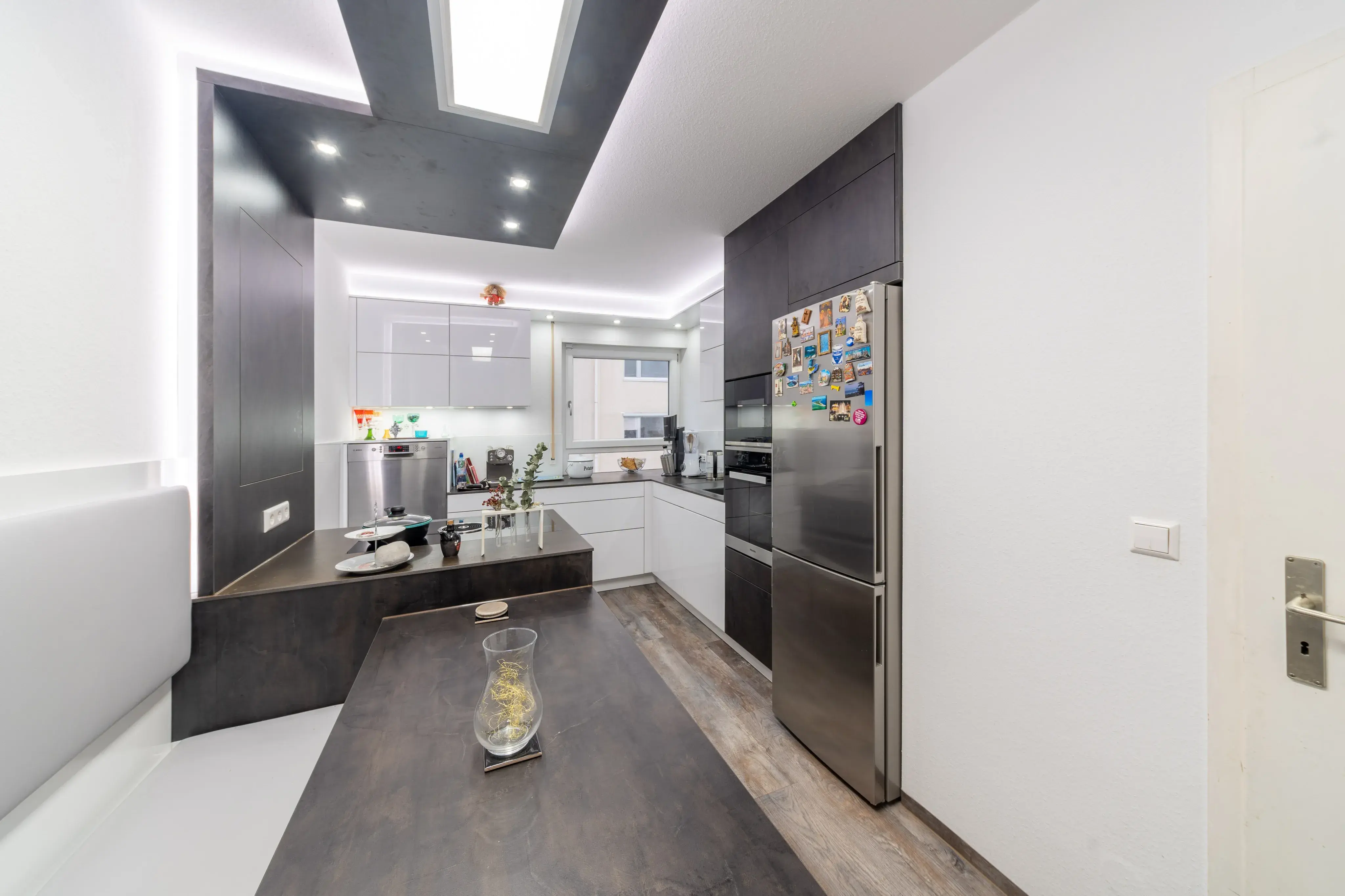 Moderne Küche mit weißer Einrichtung, dunklen Akzenten und Edelstahlkühlschrank