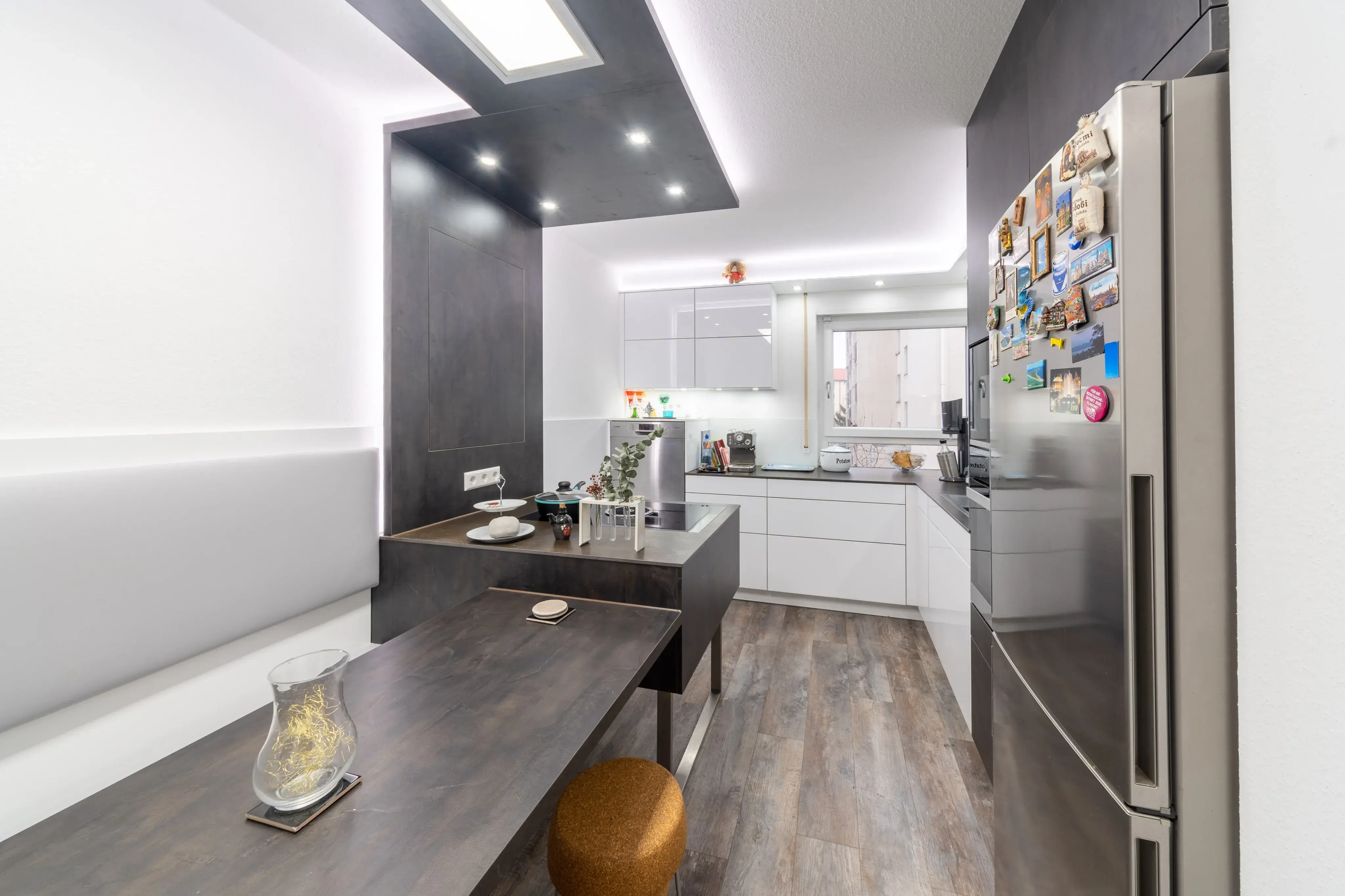 Moderne weiße Küche mit dunklem Holztisch, Kühlschrank mit Magneten und hellem Boden.