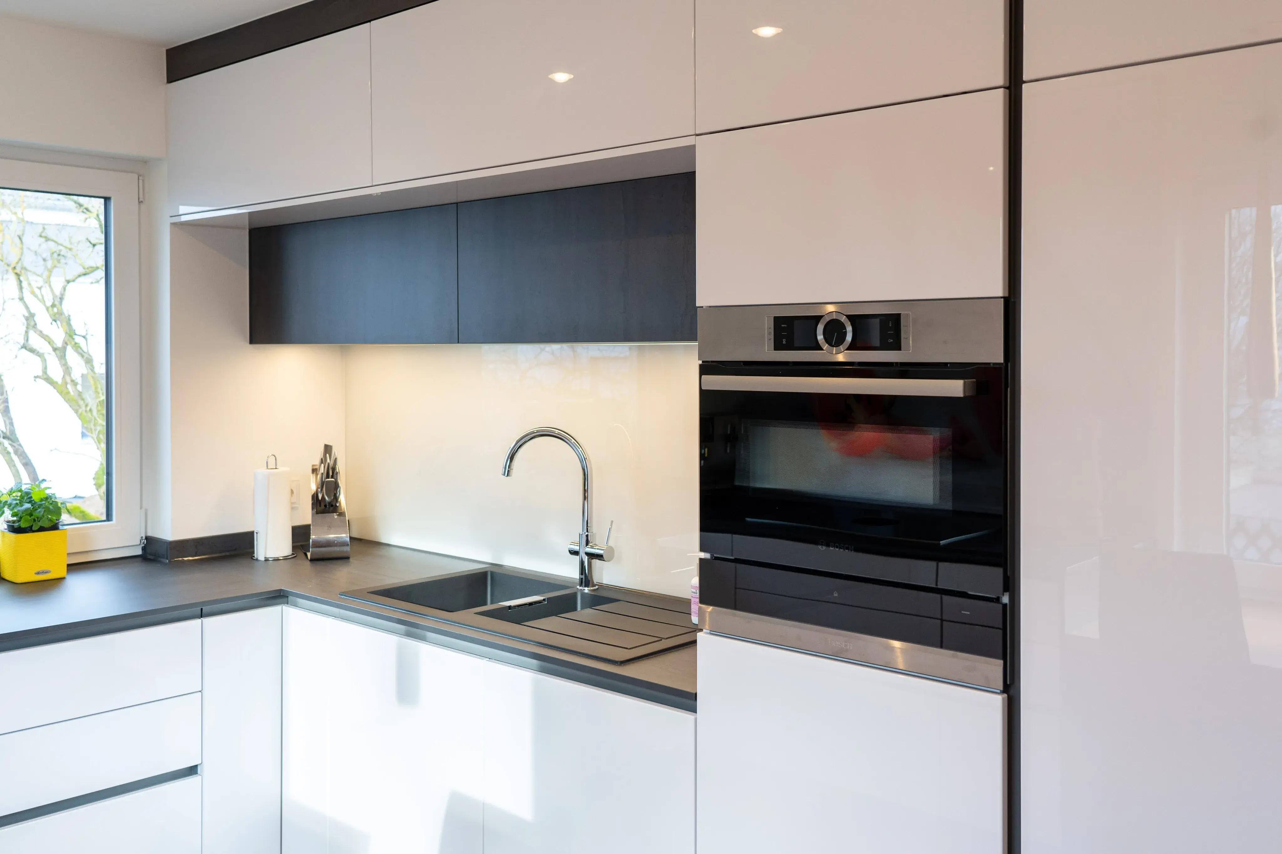 Moderne weiße Küche mit Spüle, Backofen und großem Fenster