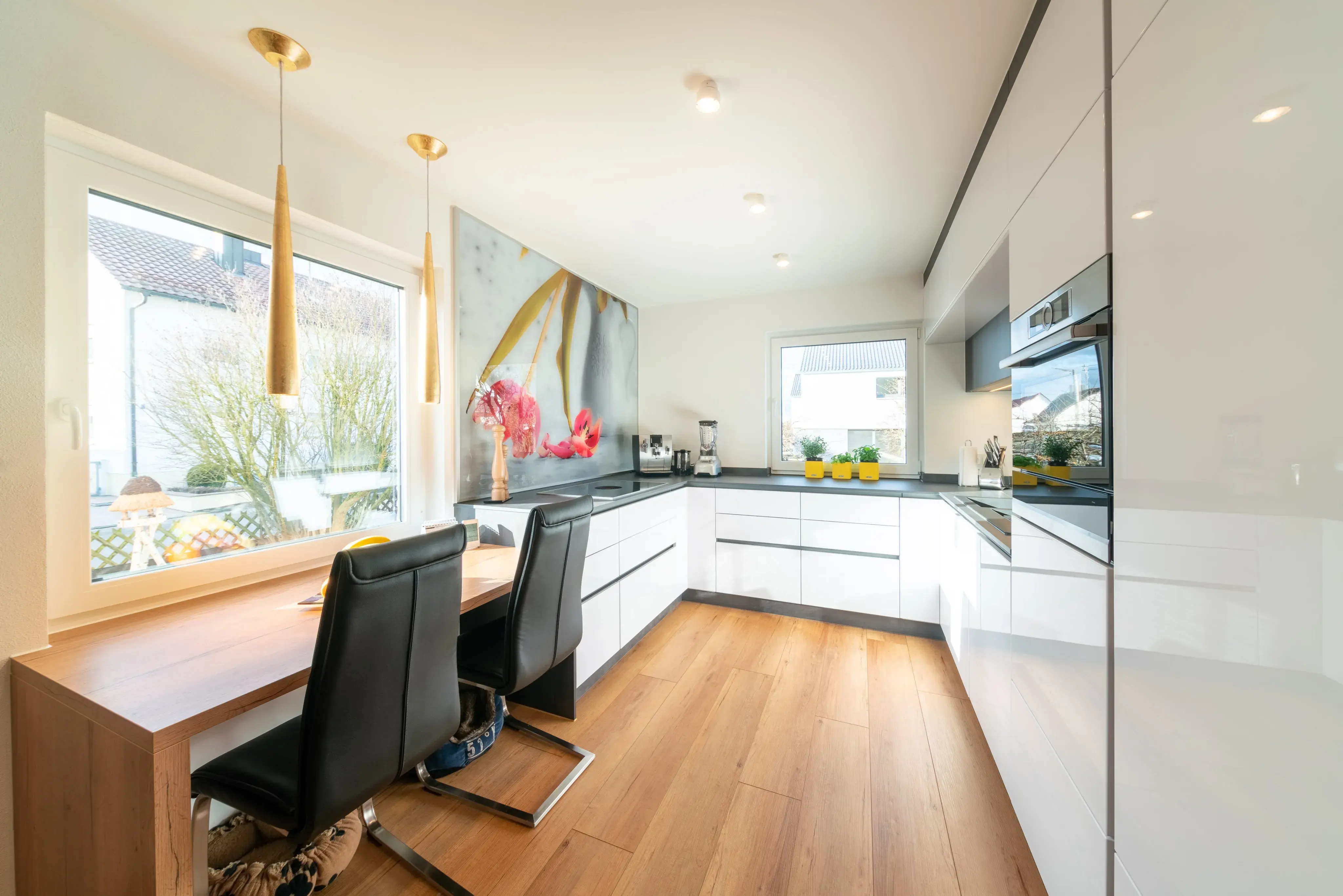 Moderne, helle Küche mit Holzfußboden und Essplatz am Fenster.