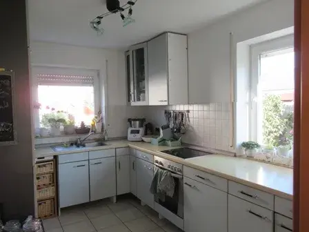 Helle Küche mit weißen Schränken, Eckfenster und Haushaltsgeräten auf der Arbeitsfläche.