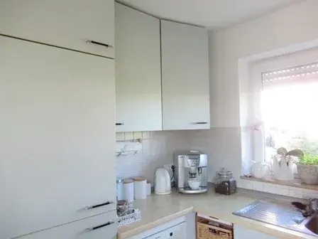 Helle Küche mit Kaffeemaschine, Töpfen und Pflanzen am Fenster.