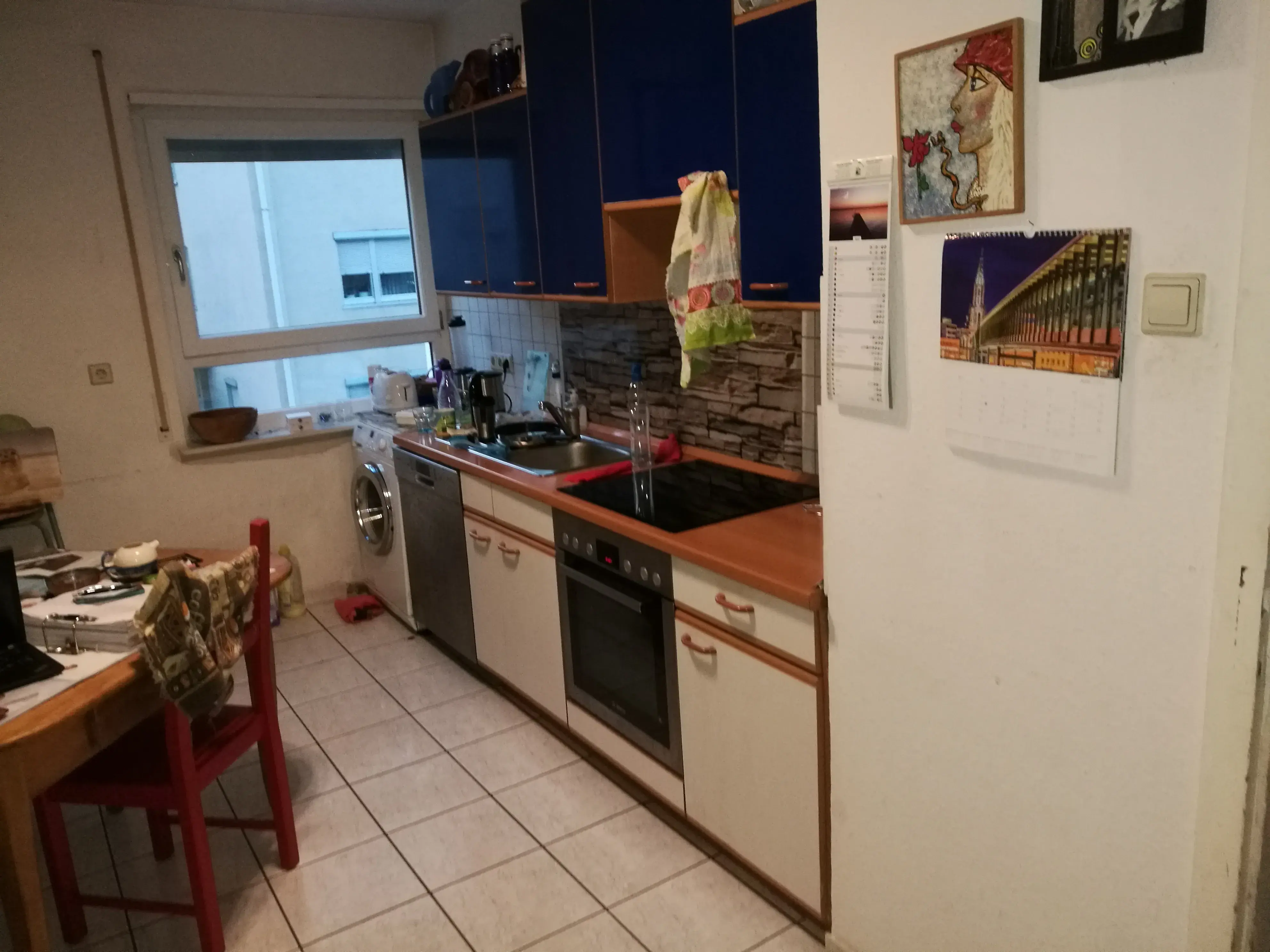 Kleine Küche mit weiß-blauen Schränken, Herd, Spülmaschine und Esstisch.