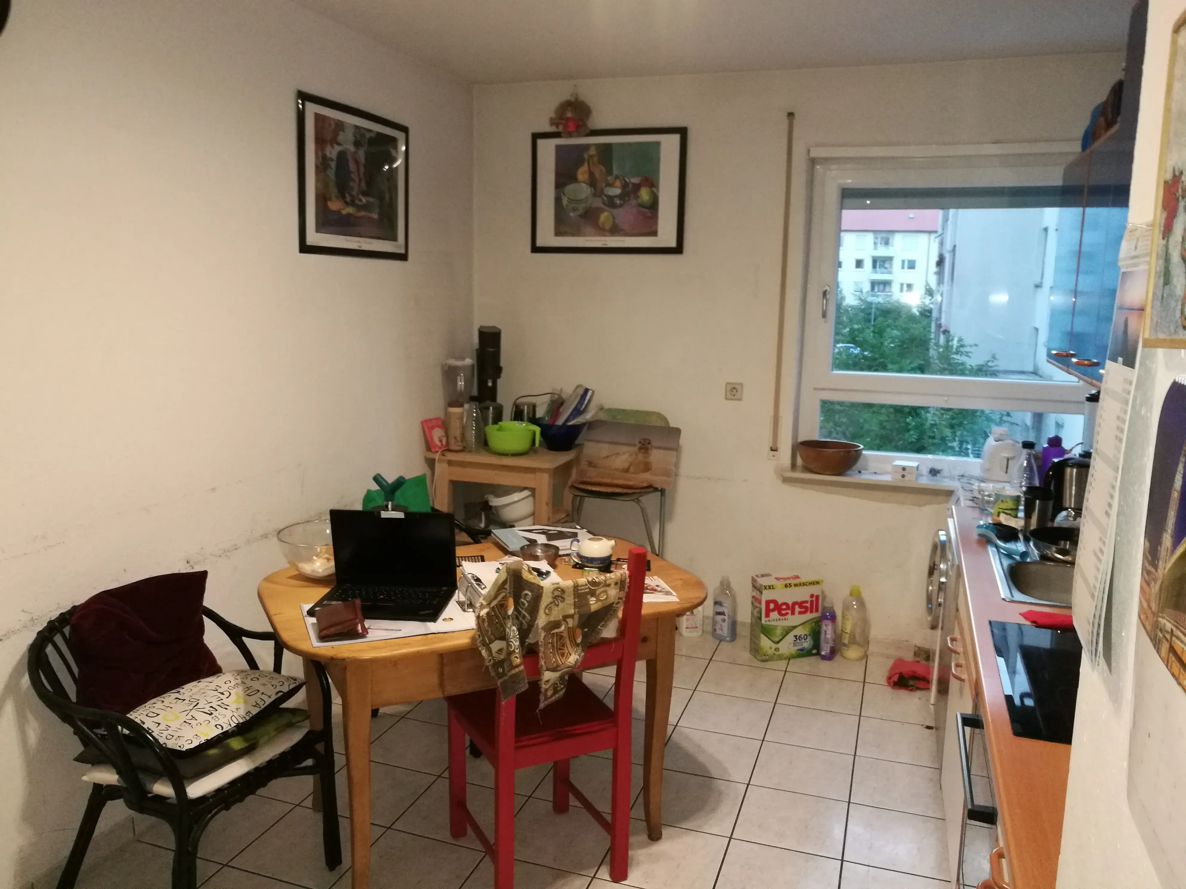 Kleine Küche mit Esstisch, Stühlen, Fenster und einigen Haushaltsgegenständen.