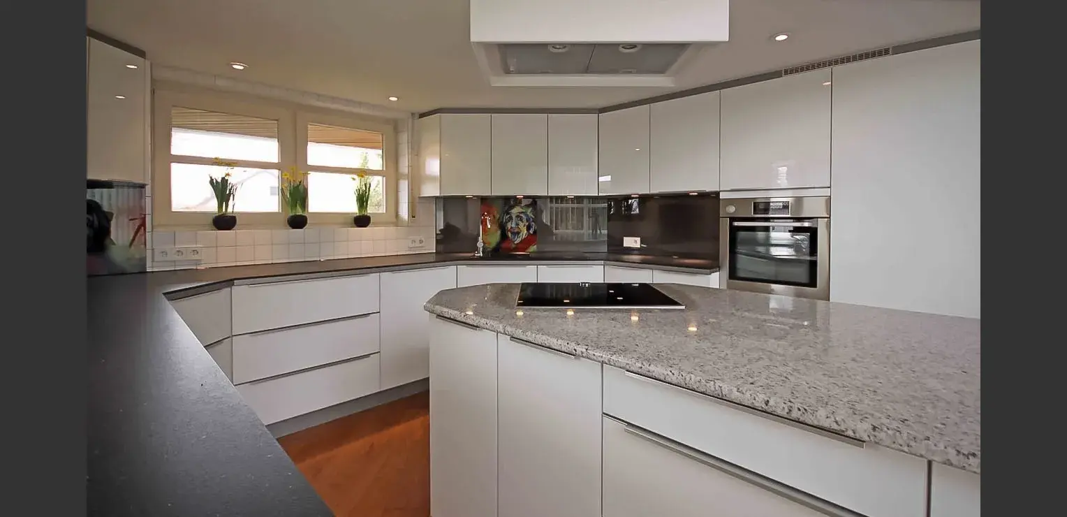 Moderne weiße Küche mit grauer Arbeitsplatte und eingebauten Geräten.